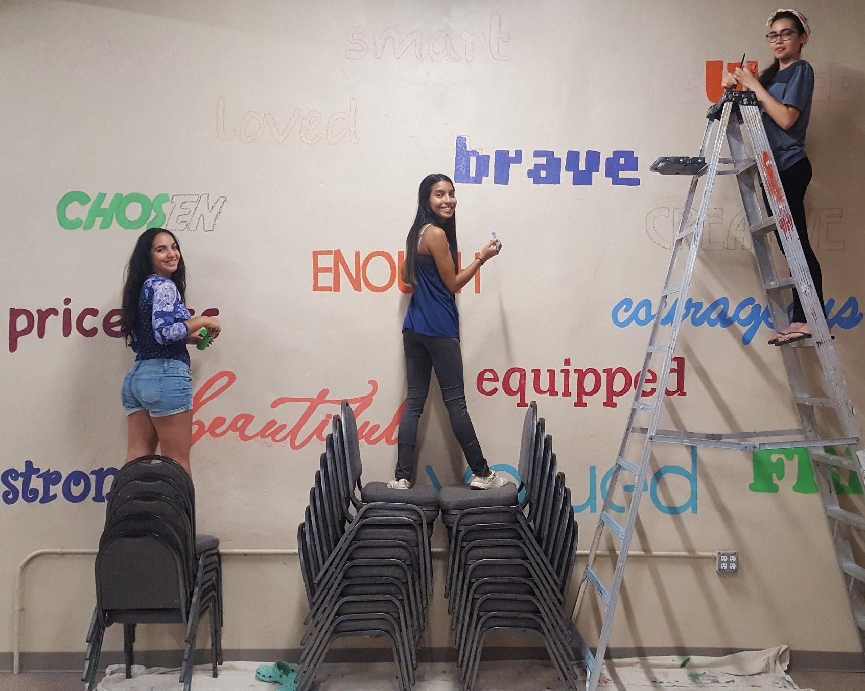 Anelys on the chairs in the middle, along with fellow interns, painting a mural at the City Light Ministry where they served children from the Reading community