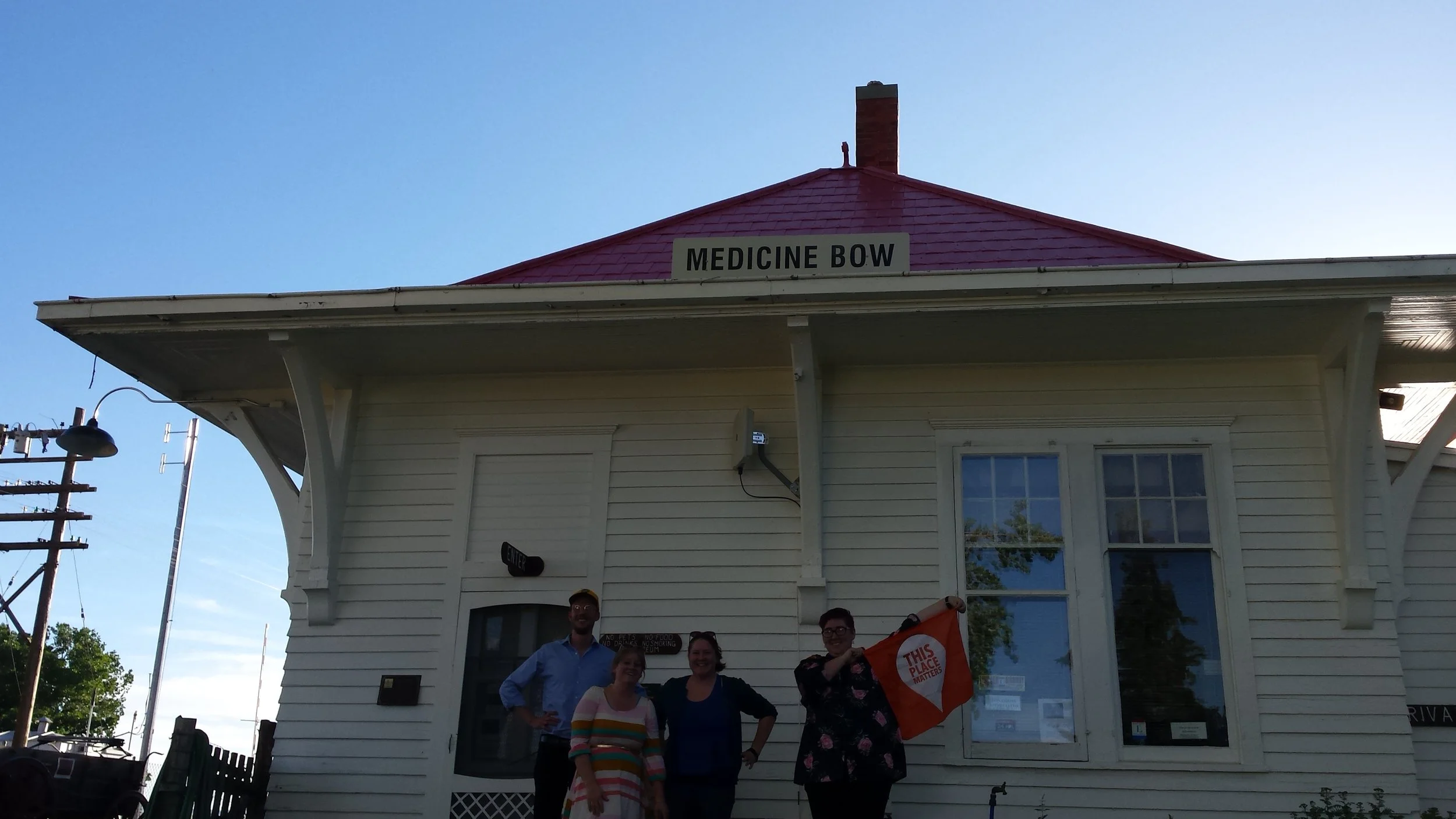 Alliance for Historic Wyoming staff pose by the Medicine Bow Depot with a "This Place Matters" banner.