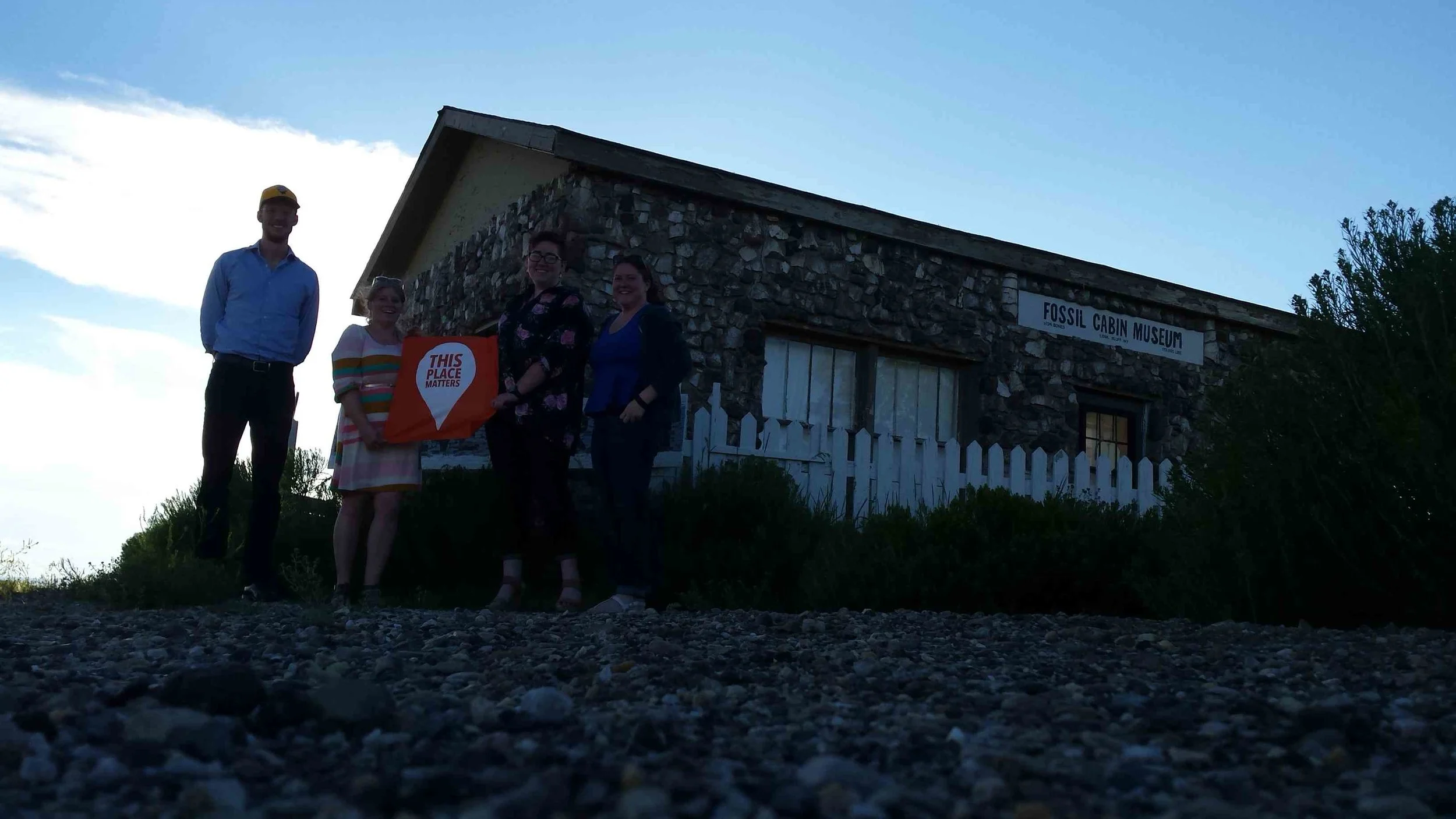 AHW staff poses with a "This Place Matters" banner in front of Fossil Cabin Museum near Medicine Bow