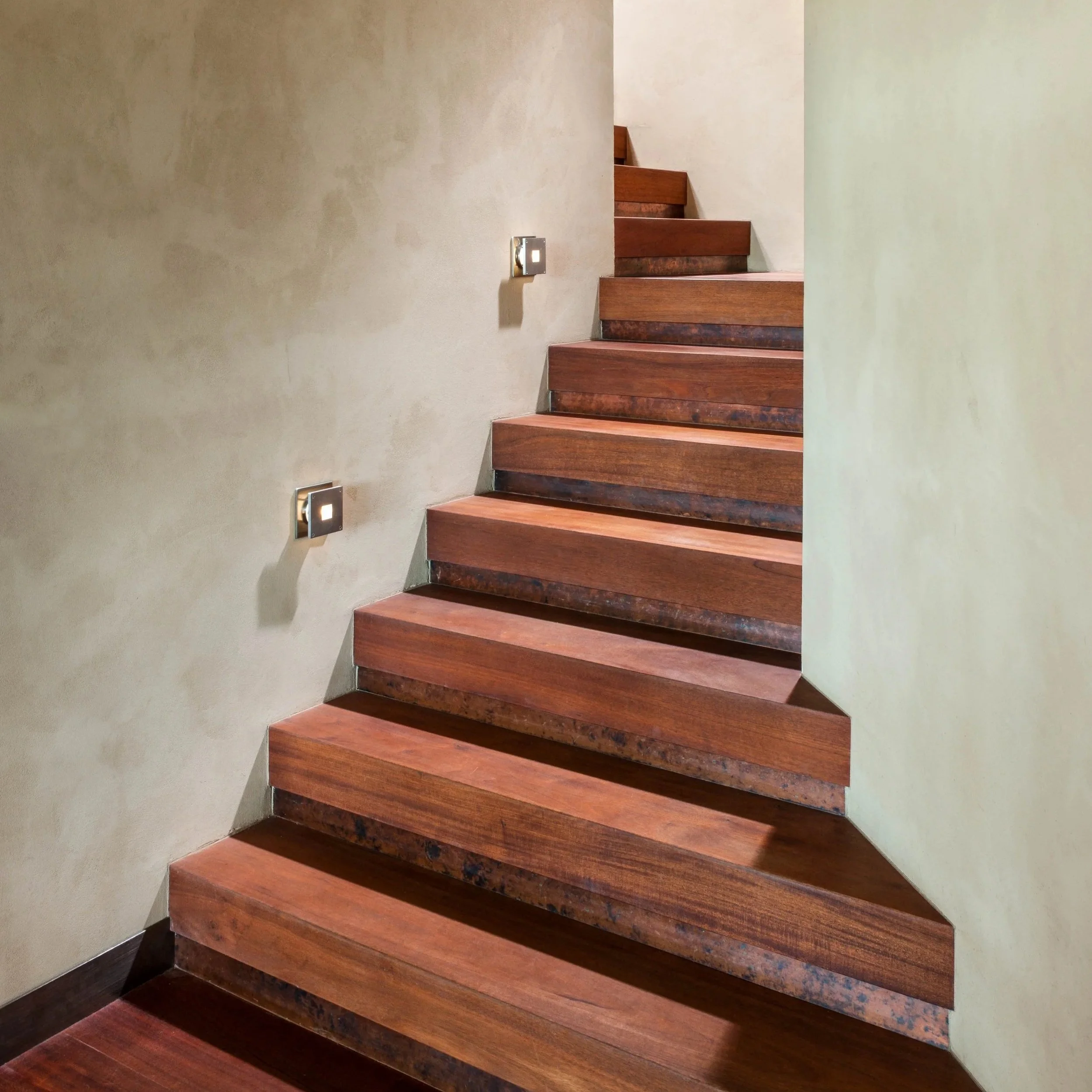 Wooden staircase next to cream-colored wall with small square wall lights