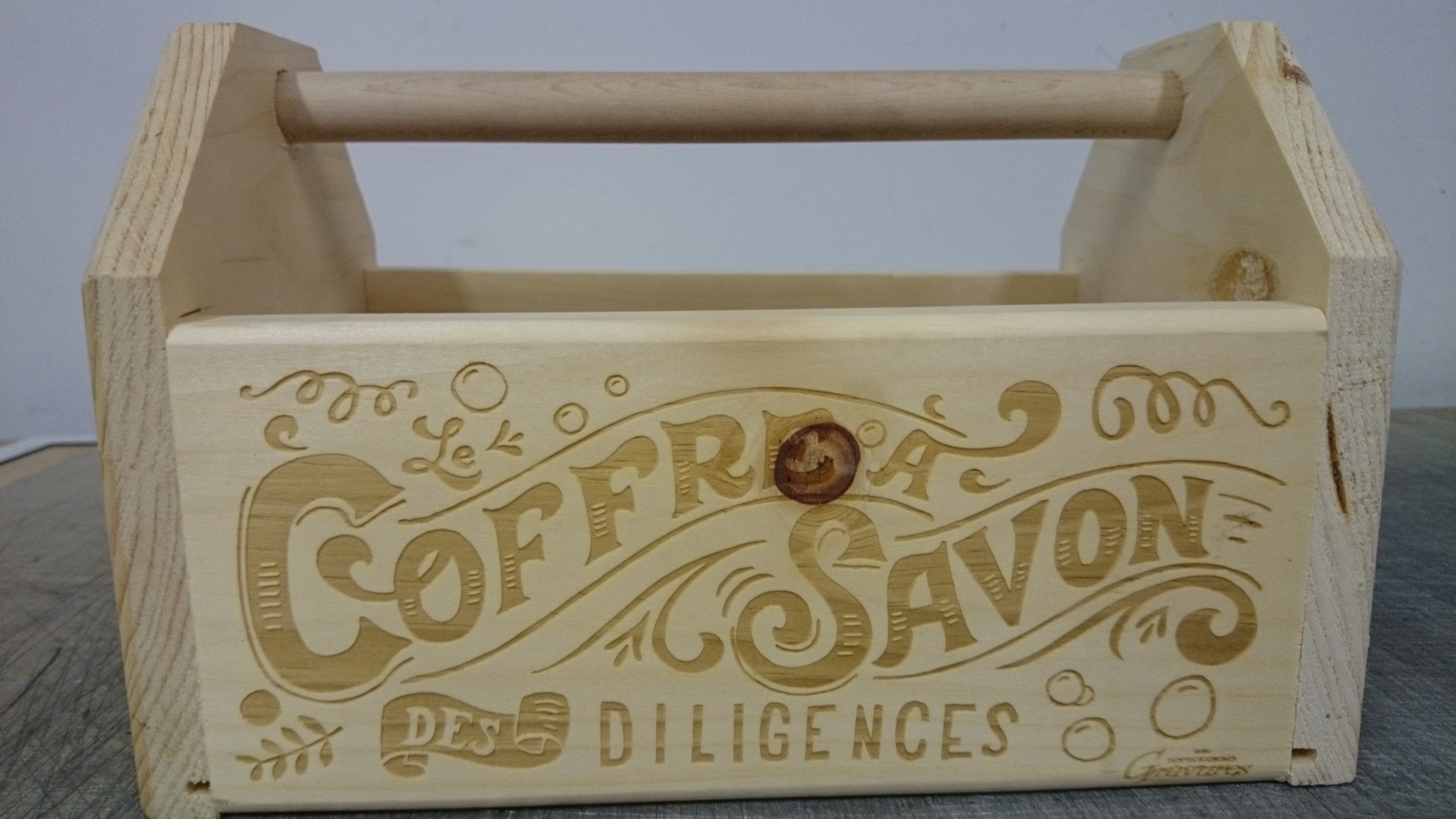 Caisse en bois clair avec poignée, gravée avec 'COFFRE À SAVON DES DILIGENCES' accompagnée de motifs ornementaux réalisé par Systa Gravure Laser