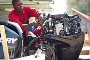 Person working on outboard boat motor near water.