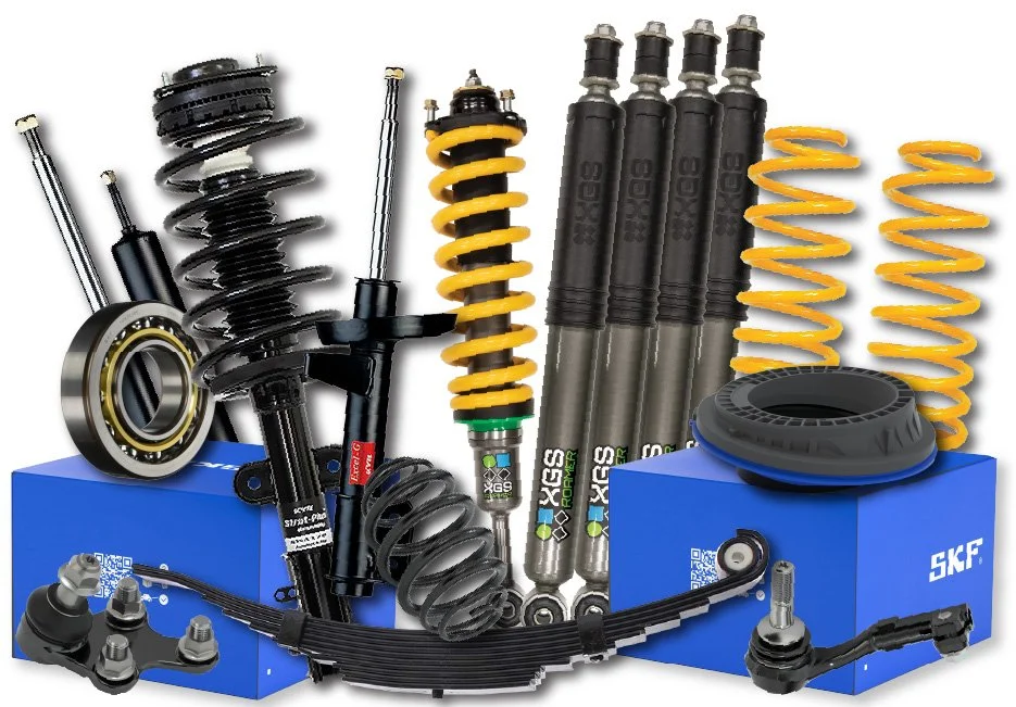 Close-up of a motorcycle tire with a tread pattern, part of the suspension system with a yellow coil spring, on a paved surface.