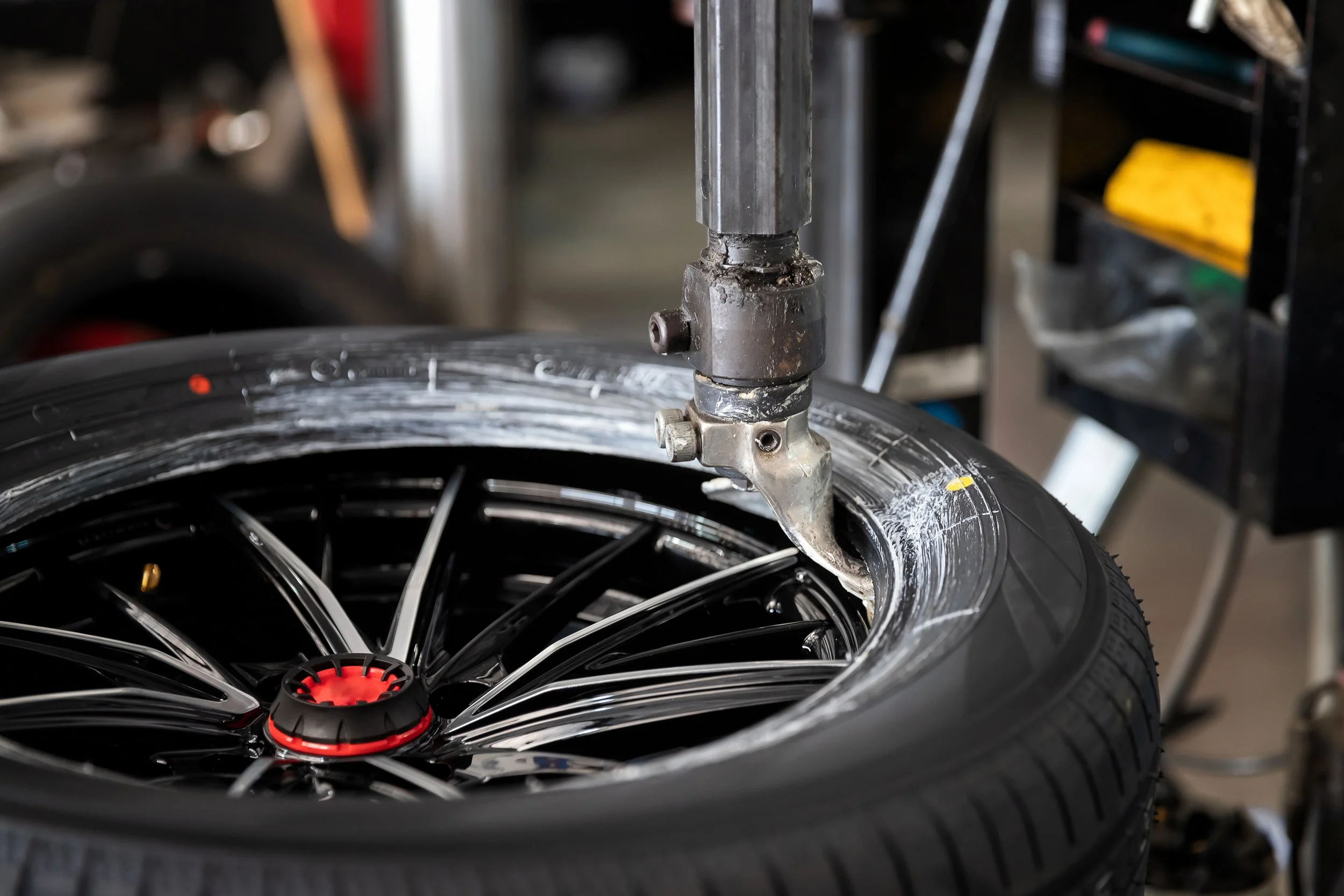 A tire mounted on a black alloy wheel with a red center cap, being worked on with a tire mounting machine in a garage or workshop.
