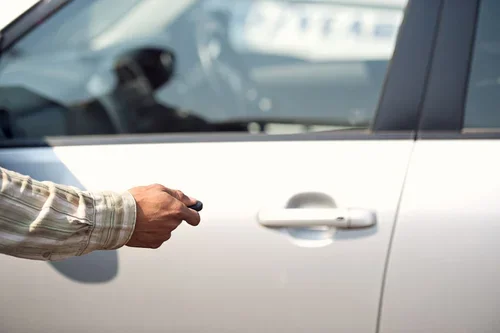Person holding a car key near a silver vehicle with a closed door.