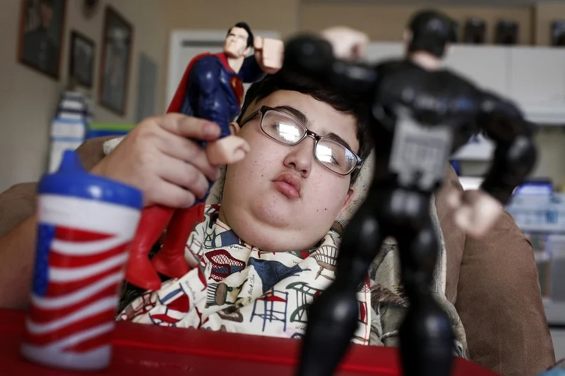 Too weak to walk on January 17, 2014, Ethan Arbelo, 12, plays with Superman action figures in a reclining chair where he spends most of his days in Lehigh Acres, Fla. “It’s heartbreaking watching your child revert,” Maria said. 