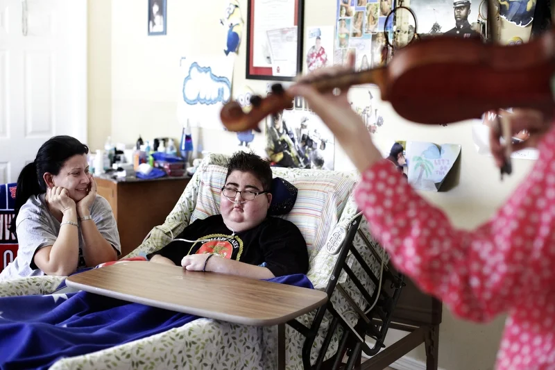 Maria Maldonado and Ethan Arbelo, 12, watch as violinist Nanette Grant plays a private concert on June 12, 2014 in Lehigh Acres, Fla. “I’ll do anything to get his spirits up,” Maria said.