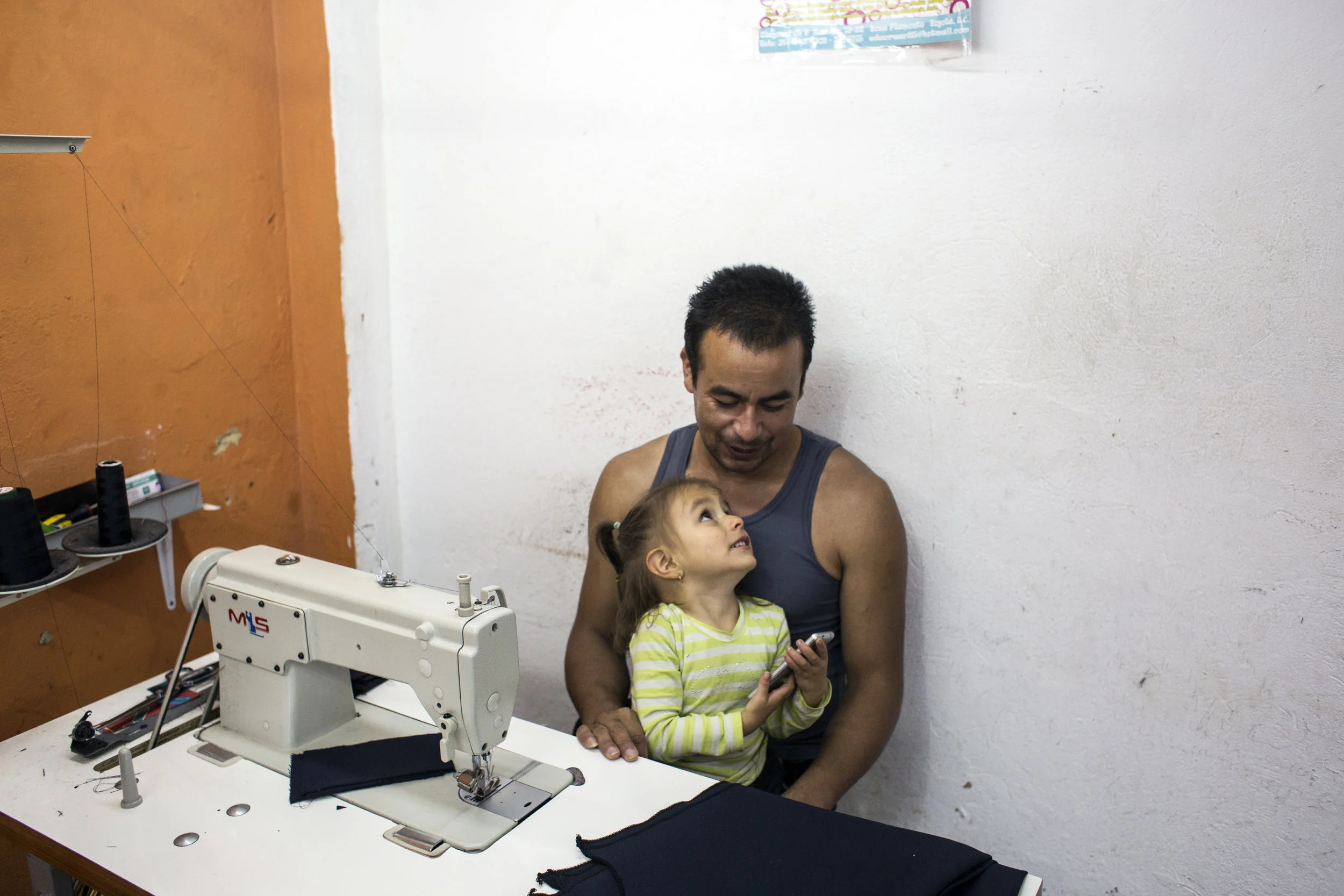 Milton Hernandez, 33, sits with his daughter, Dana Sofia Hernandez, 3, while at his clothing business, where he sews pants and jackets for a brand on September 21, 2016, in Bogotá, Colombia. Hernandez was 19 when he joined the FARC and demobilized 10 years later, after losing a leg to a grenade. He says he had a rough start integrating back into society but is happy he is financially stable and working for something he enjoys. 