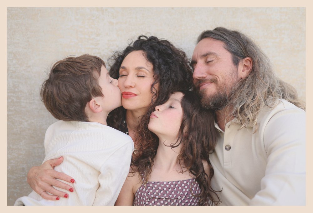 Family of four, a mother, father, and two children, sharing an affectionate moment with eyes closed and faces touching.