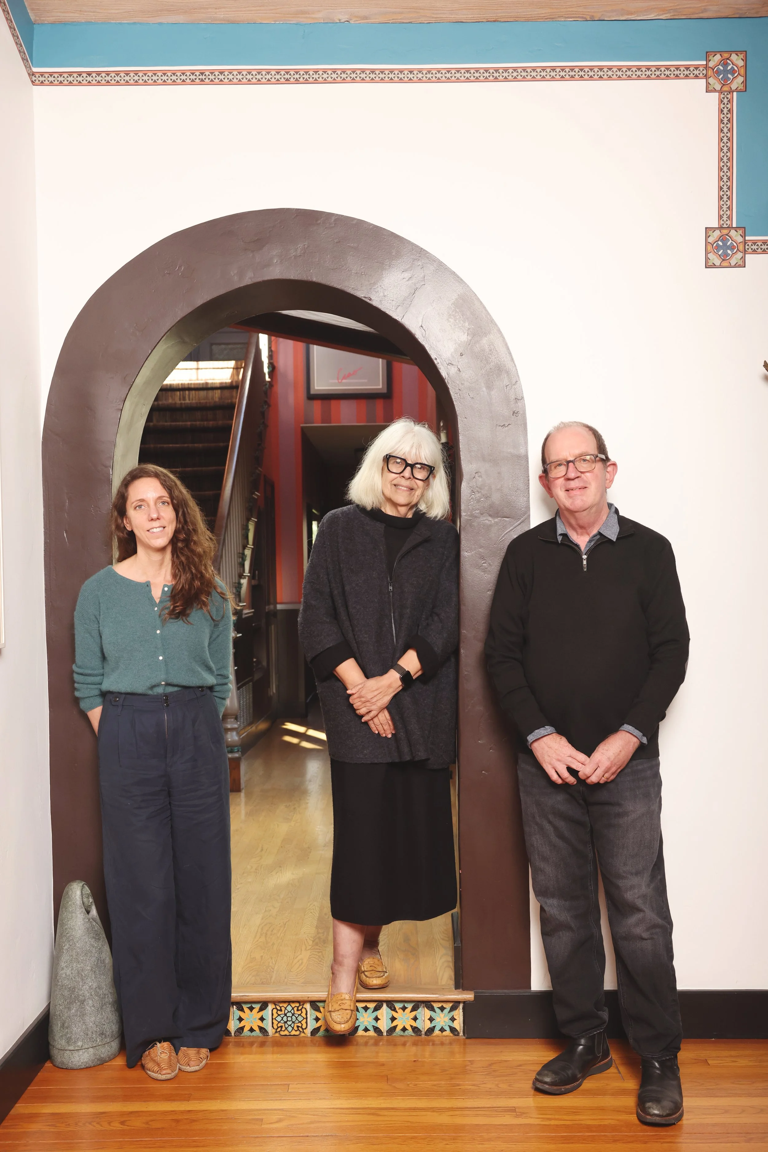 Three people posing beneath a large arched doorway with colorful decorative tile trim.