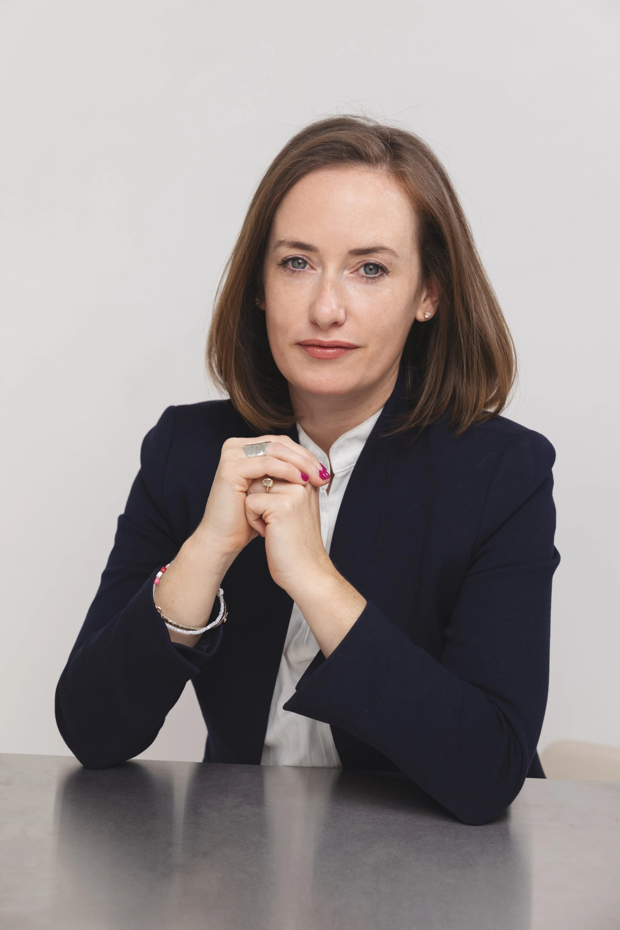 Professional woman in a navy blazer resting her chin on clasped hands at a desk