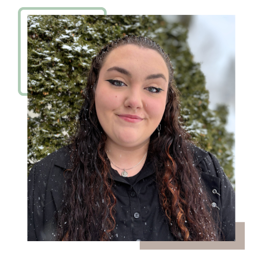 Picture of Madysen, a white, fat, pagan, acespec, Autistic, femme lesbian. Madysen has long brown curly hair and is wearing a black button up shirt. They are standing in front of greenery.