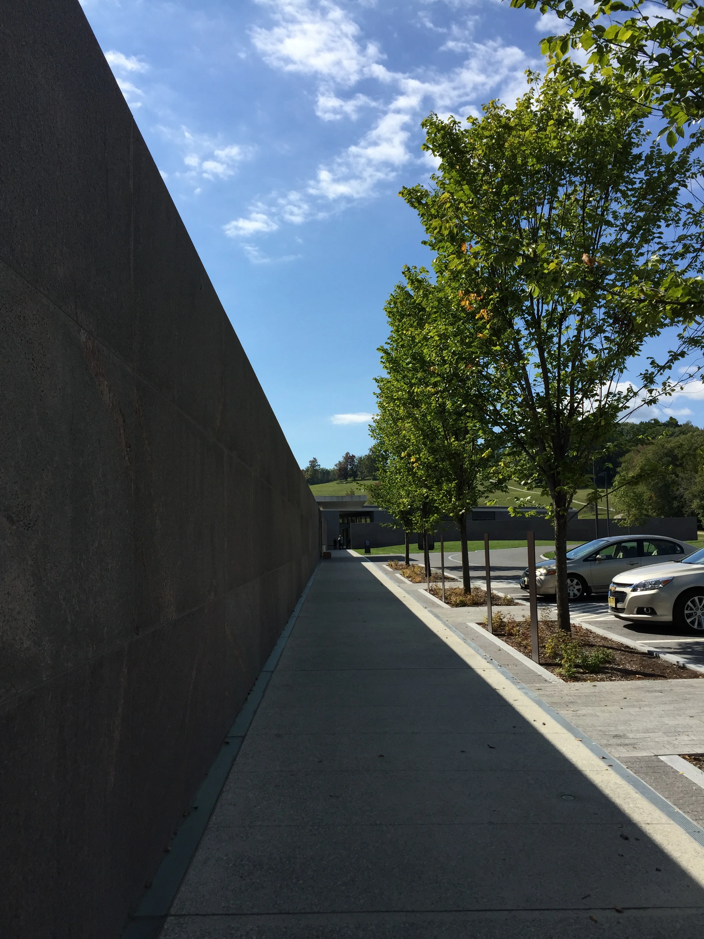 An extended red granite wall draws visitors down a long line of procession from car park to entrance