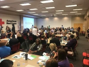 "The Cincinnati/ Hamilton County Continuum of Car e (CoC) was built on a framework of collaboration, community process, and shared decision-making. Strategies to End Homelessness, as the CoC lead, is responsible for upholding the shared vision of the community and facilitating a system where no one entity determines our path. https://www.strategiestoendhomelessness.org/building-a-system-with-community-voice/ # Expertise lives at every level of the system – in direct service to our clients, in data collection and evaluation, in project administration, in compliance, and in macro-level system planning. And the uniqueness of our community is that all expertise is valued and no single person or agency’s perception is more important than another. The system only works because of the variety of skills we hold. Community process happens at Strategies to End Homelessness on a regular basis via open work groups, community strategic planning sessions, and most notably, annual funding allocation processes. On Friday, June 30th, STEH facilitated our annual Large Group Scoring event; a full-day of prioritizing housing and service projects for inclusion in the annual Continuum of Care application. Nearly 150 community members invested in the homeless service system came together to review project performance, hear presentations, and rank more than 30 separate projects to determine a community prioritization list which will result in the allocation of almost $17 Million. While I know that the Large Group Scoring event can cause some anxiety among the people responsible for making presentations, I hope they see the value in the transparent prioritization process. Personally, it’s one of my favorite days of the year! In 8 hours, we are afforded the opportunity to hear about all of the amazing work that is happening in our community. And in a system where the need for our services is so abundant, accomplishments can often be overlooked. Thank you to all of the CoC service providers for the work that you do every single day and for participating in our community processes to make our system work. Your participation is invaluable to the success of our community. As the CoC Director for STEH, I look at all of our work with a critical eye on how to build in community process. This is something that I find somewhat challenging to explain to other communities because quite frankly, it would be simpler to identify a small group of decision-makers to decide the next steps of the CoC. But, community voice builds investment in the system, and keeps us progressing. While Large Group Scoring only happens once a year, the philosophy of collaboration is interwoven in all of the work that we do and will always be the framework for the success of our homeless service system. And finally, thank you to the American Red Cross for use of their great community space, Cincinnati Cooks for catering a delicious lunch, and all of the Strategies to End Homelessness staff for your work to make our largest event of the year run so smoothly!"