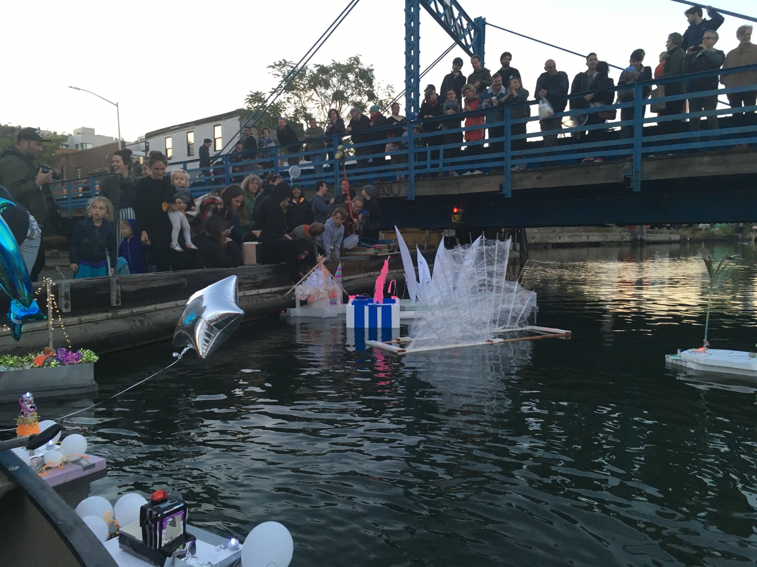 A crowd gathers on a bridge overlooking the Gowanus art flotilla.