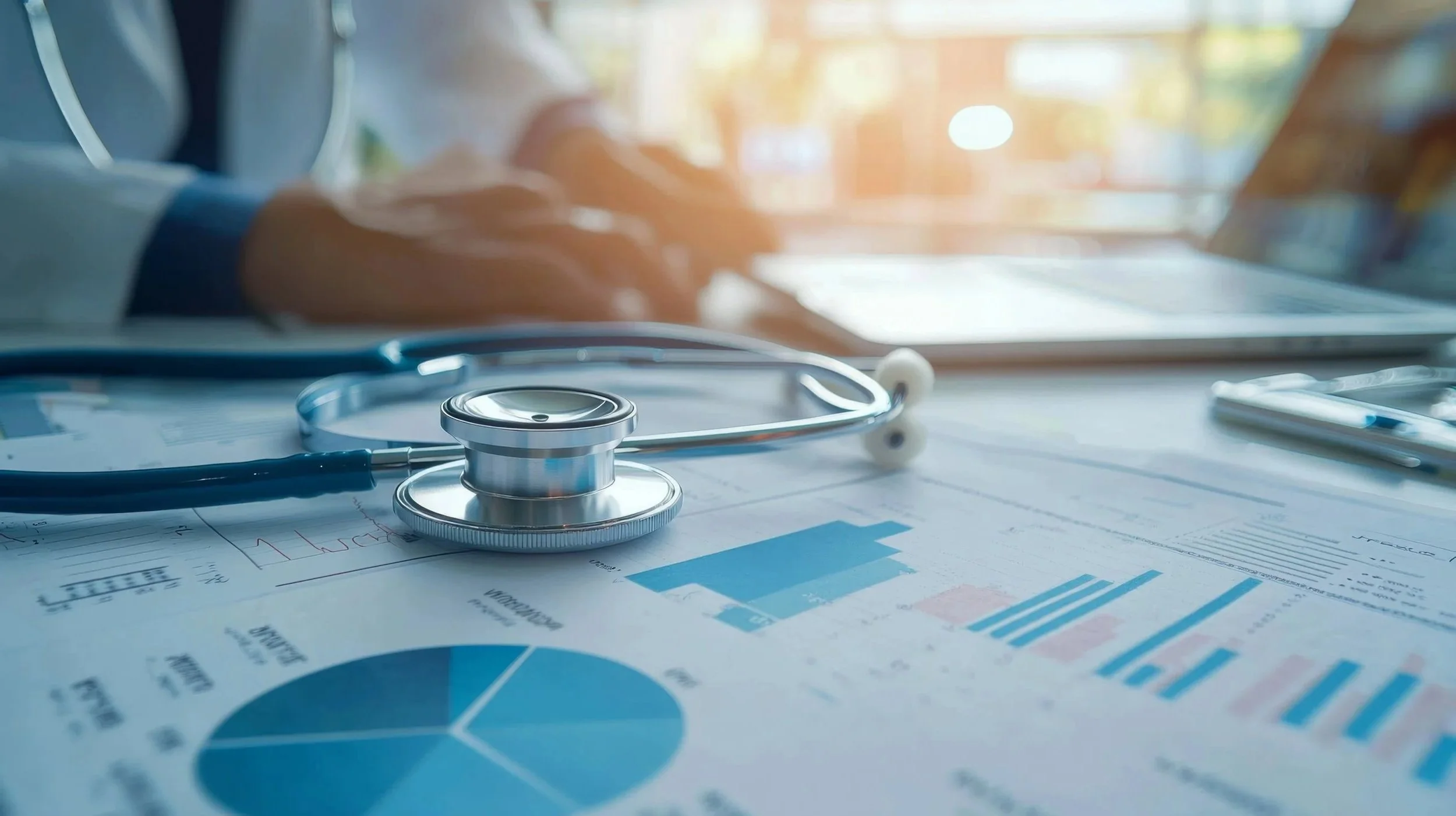 Close-up of a stethoscope resting on financial charts and graphs, with a healthcare professional working in the background.