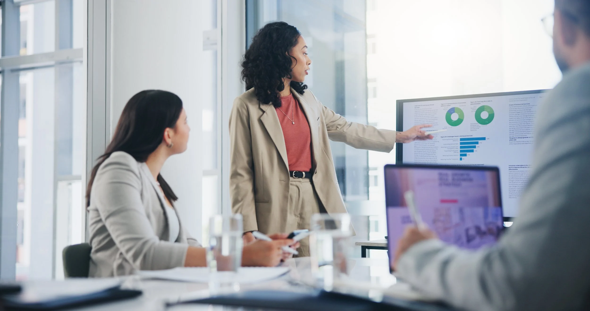Businesswoman presenting data on a large monitor to colleagues in a modern conference room.