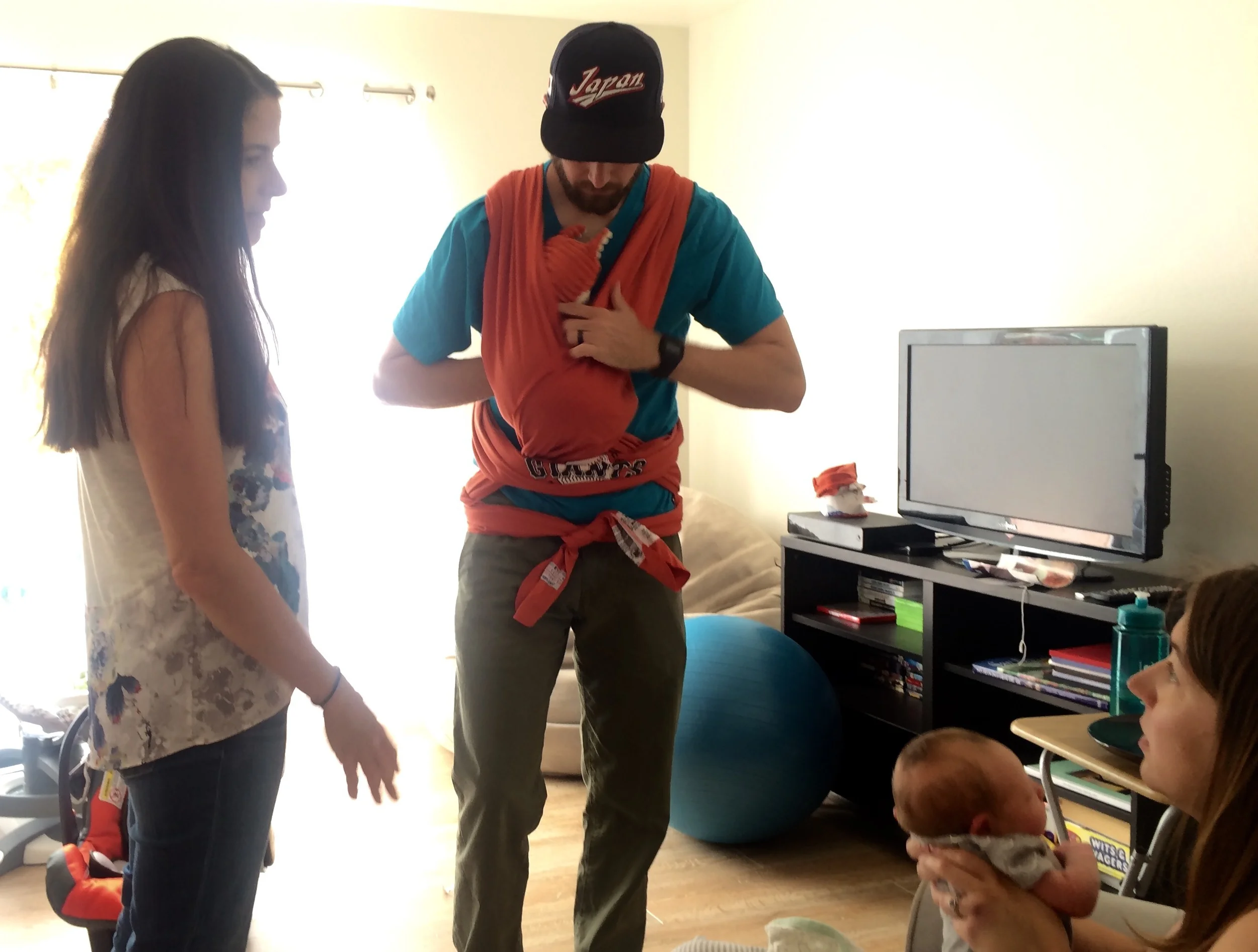 Dad learning the art of baby wearing in the Moby as mom looks on
