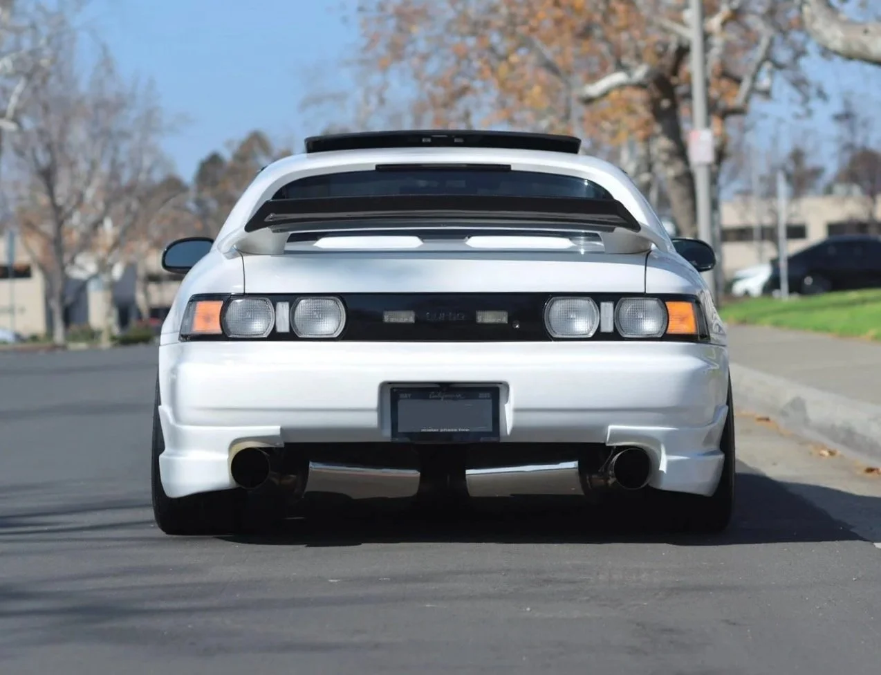  The rear bumper uses  Border add-ons  to extend the lower body line, and the spoiler has a  POON SW20 carbon-fiber rear add-on  that came from Thailand. The exhaust exits through a pair of  TCS high-flow mufflers , which helped give the rear the sym