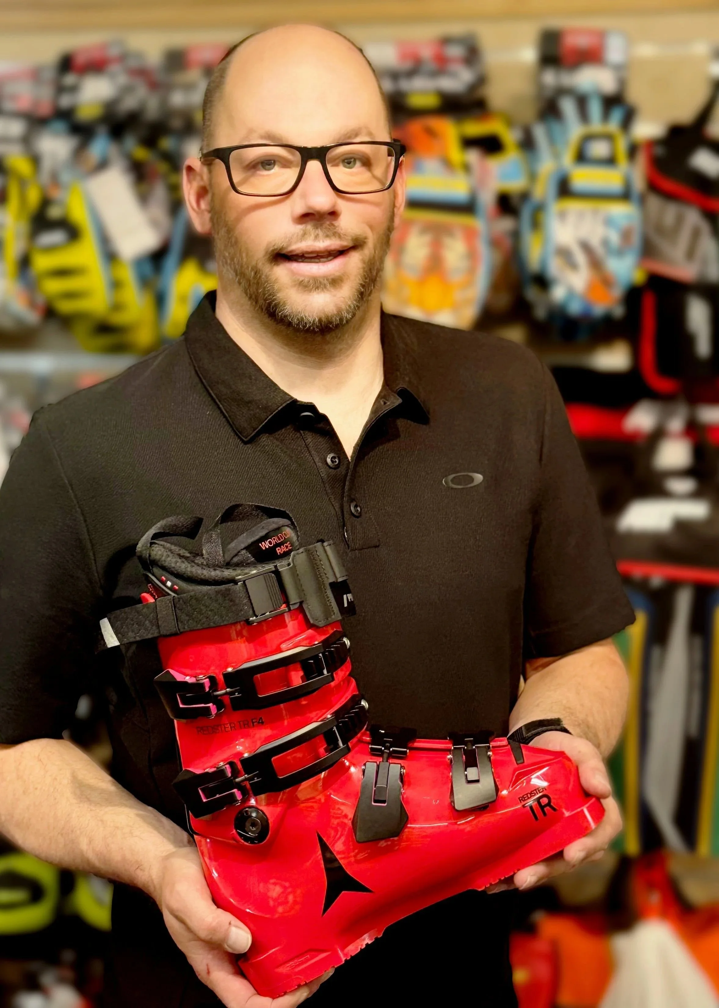 Man holding a red mountain biking shoe with black buckles inside a store with various shoes on display in the background.