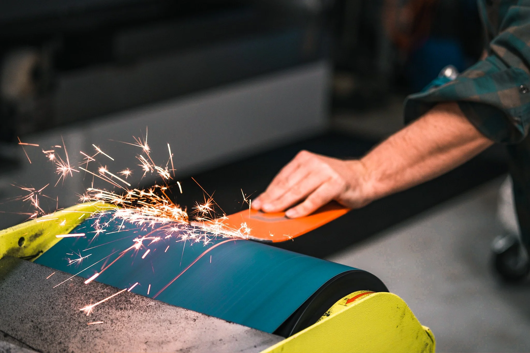 Close-up of a worker's hand welding on a piece of metal with sparks flying around in a manufacturing or industrial setting.