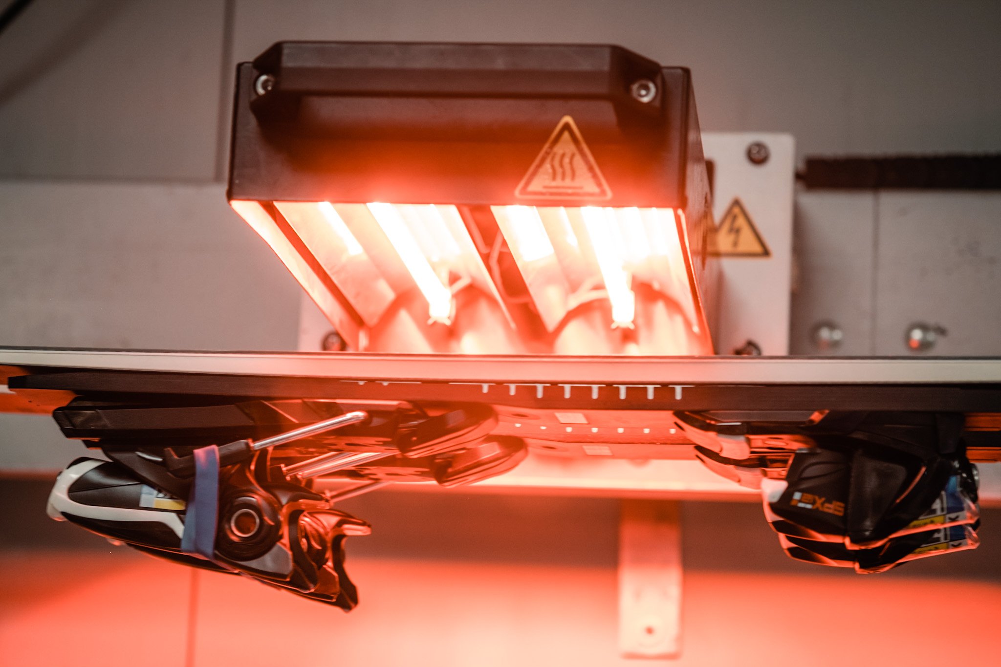 A 3D printer emitting orange light as it builds a model, with parts of the printer and some electronic components visible.