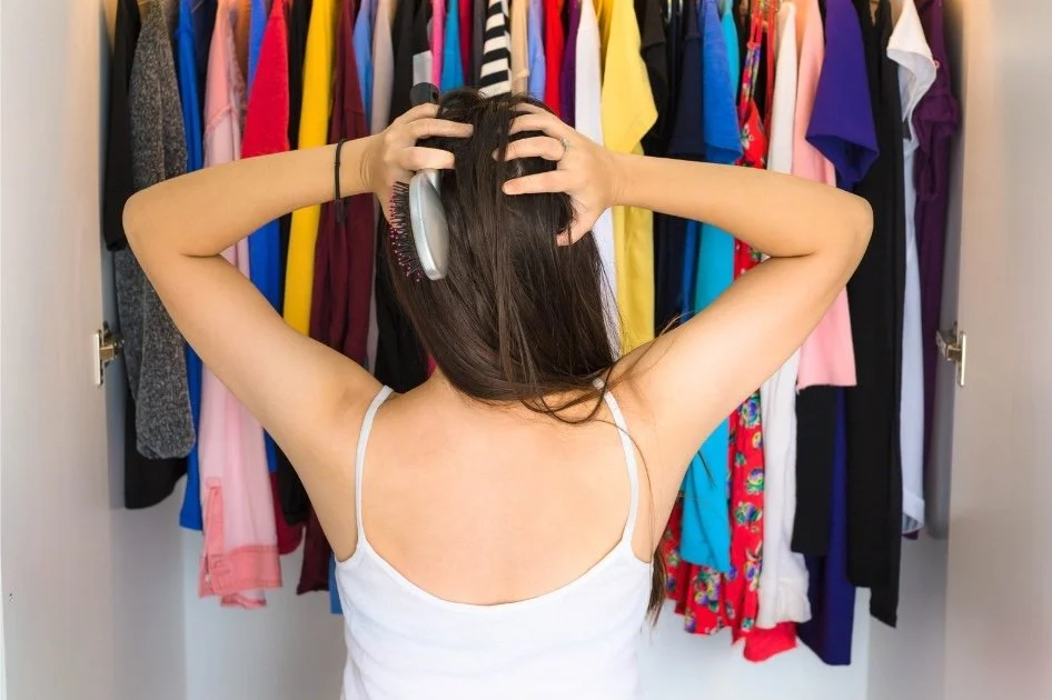 Woman standing in front of closet, hands on her head in frustration.