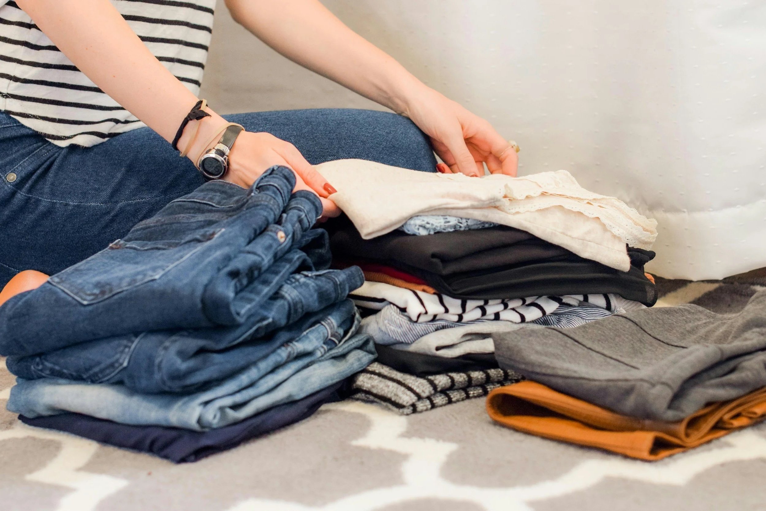 Woman kneeling on a rug, sorting folded clothing.