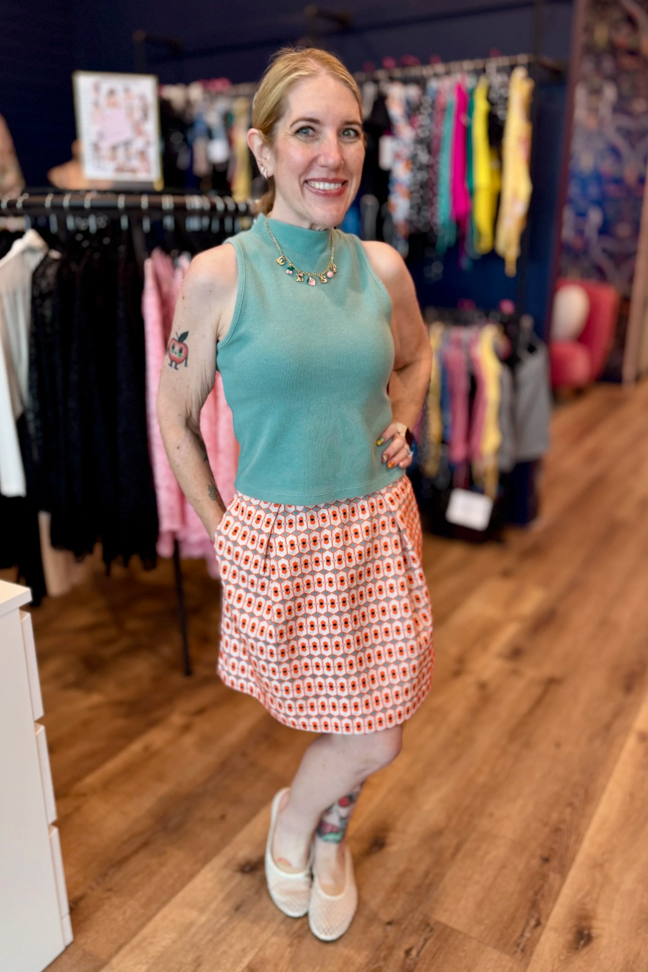 Jill Swensen standing at work, wearing a thrifted sleeveless sweater and pleated graphic skirt