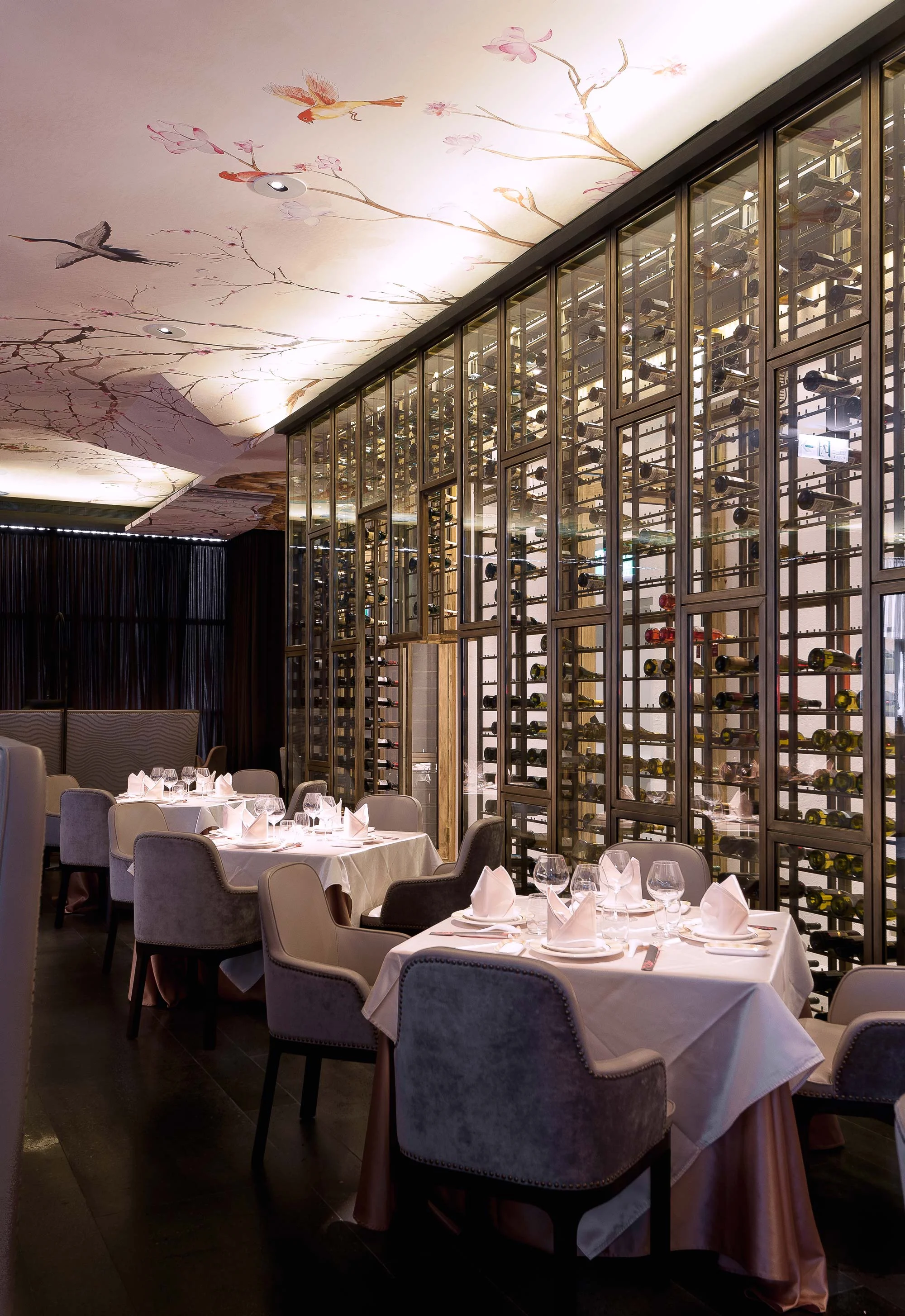 Restaurant interior featuring a wall-sized wine case, bespoke tables and chairs crowned with a China-inspired hand-painted artwork on the ceiling