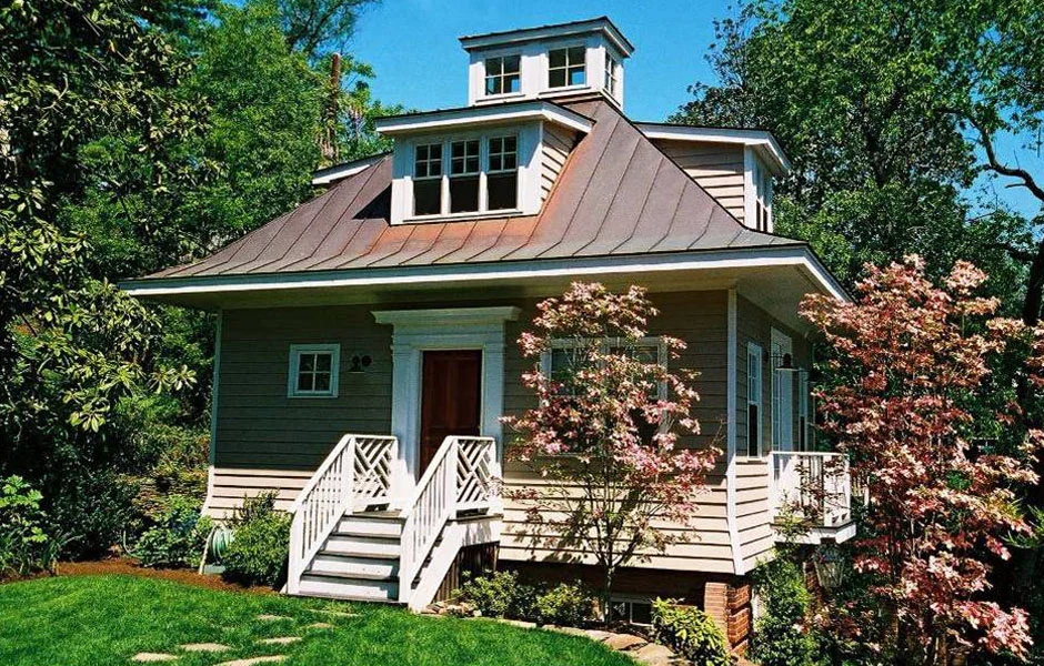 This new 1,090 square foot guesthouse and home office is constructed on the site of an old garage, accessory building on the family property in the Belle Haven neighborhood of Alexandria, Virginia. The new guesthouse is nestled into a hillside on the property, allowing what is effectively a two and a half story structure to appear much smaller, especially as it faces the existing residence. Guesthouse functions are divided by floor. The lowest floor houses a family or movie room with a large screen projector. The second floor and main entry level is the main guest quarter, while the third floor houses a home office. The office floor in the roof and benefits from ample light gathered by dormers on all four sides of the structure, and from above through the cupola. The architectural form of the guesthouse takes subtle cues from the main residence. Large overhangs and a distinctive roof line give the simple design a unique character. The guesthouse is constructed of brick, stone, clapboard siding, and copper roofing. Windows are painted wood with true divided light glass. 