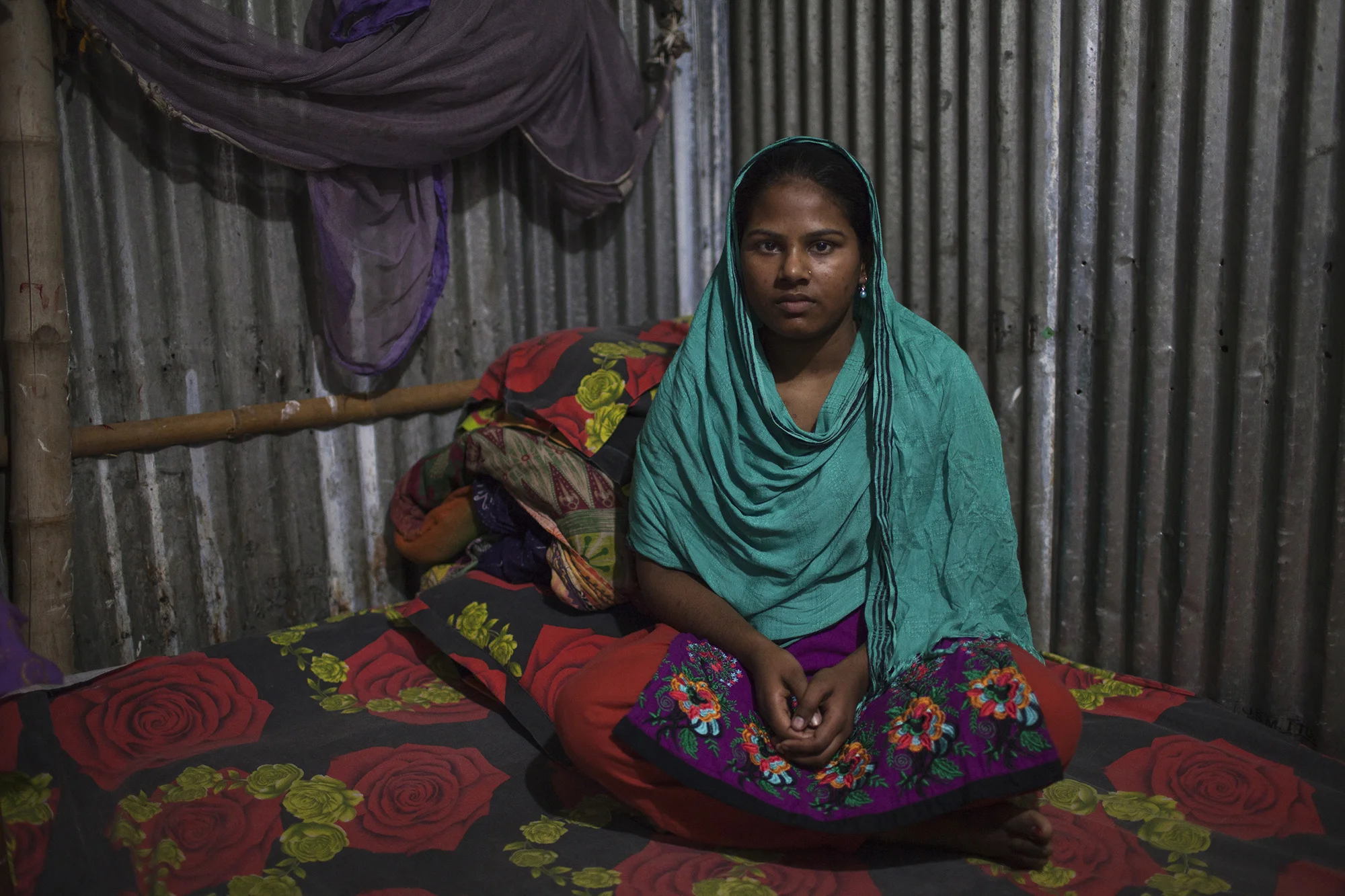 Garment worker Semu Begum, 22, who works for Lifestyle Fashions Maker Ltd, sits on the bed inside her rented room in Dhaka, Bangladesh. (Credit: Will Baxter)