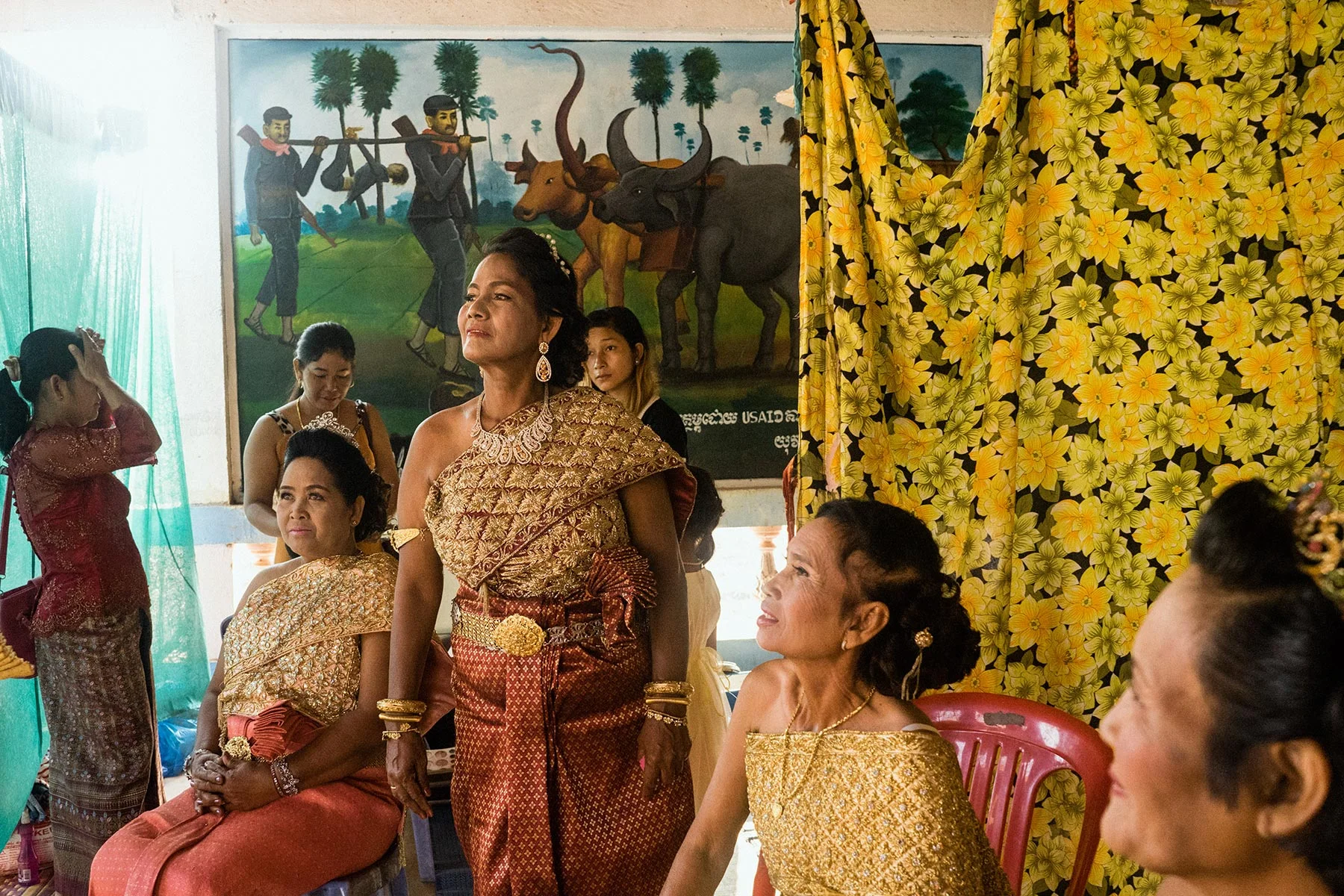 As they get ready for the remarriage ceremony, some of the brides sit in front of a mural illustrating war crimes carried out by the Khmer Rouge. 