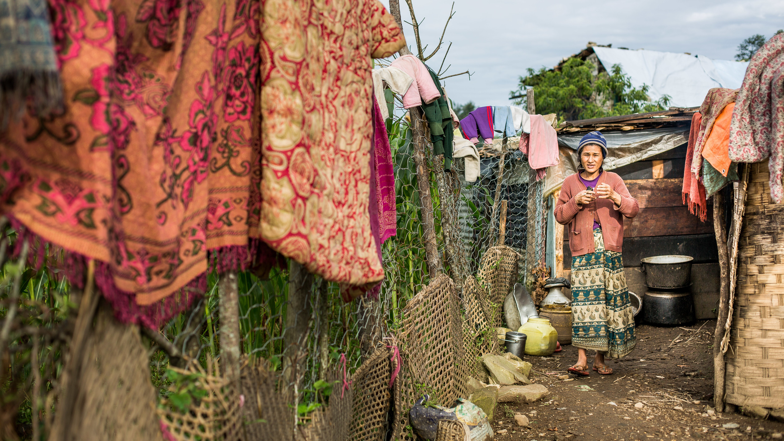 Women living in her plastic shelter that is too small to store all the family clothing and blankets.