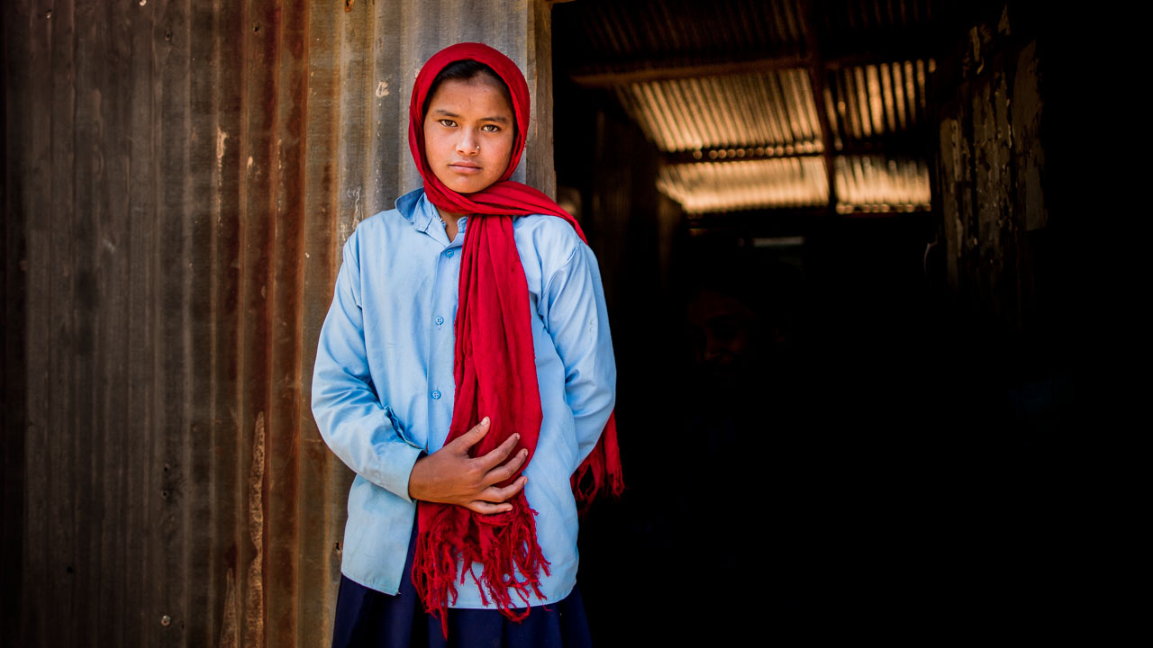 Girl standing in front of her temporary tin classroom. 