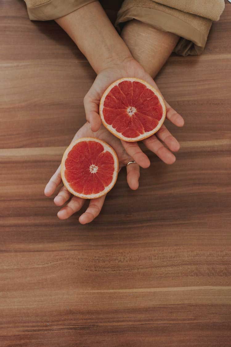  Two crossed hands showing 2 halves of a red orange. 