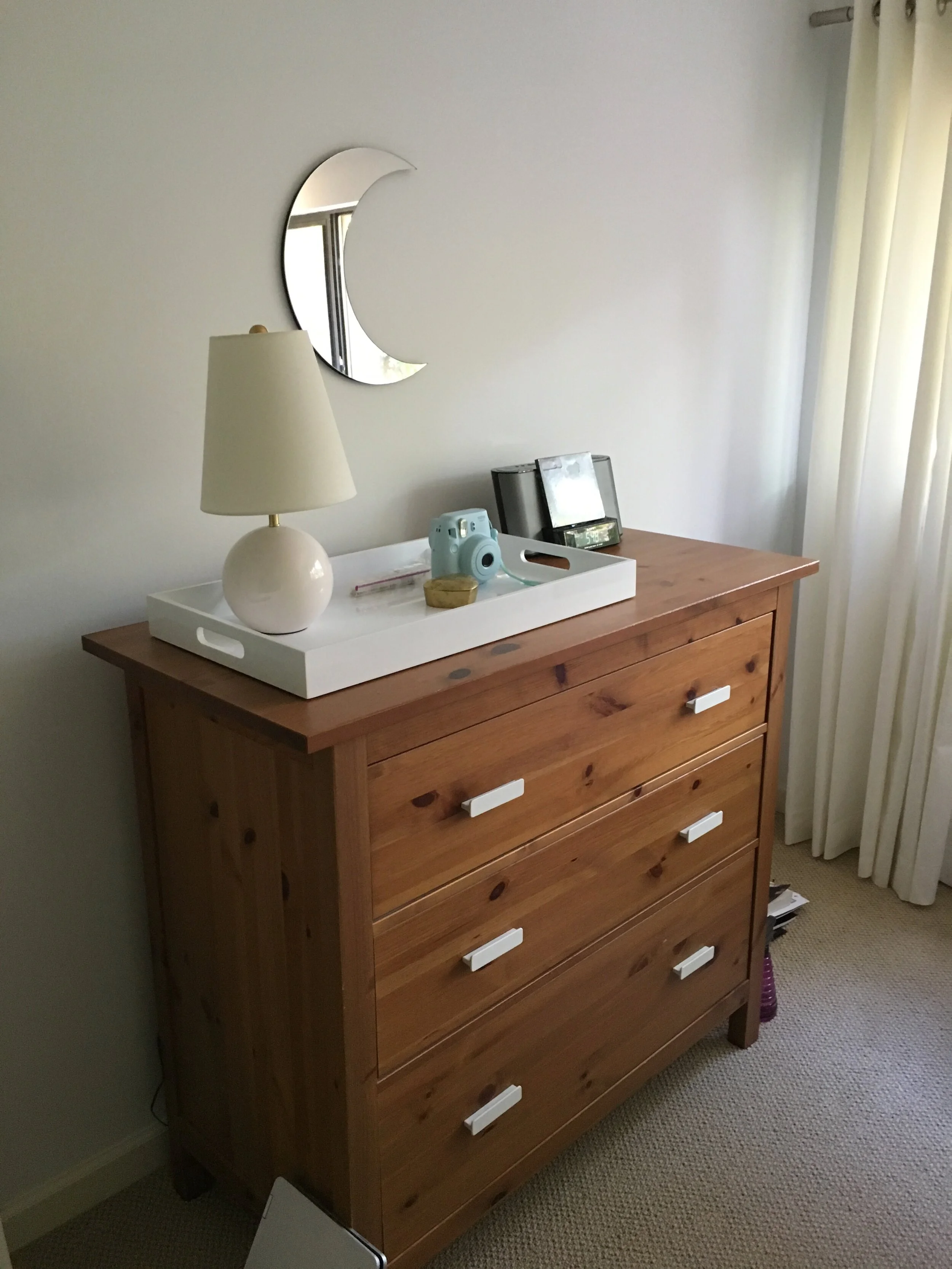 Wood dresser with new white drawer pulls with moon mirror and white tray.