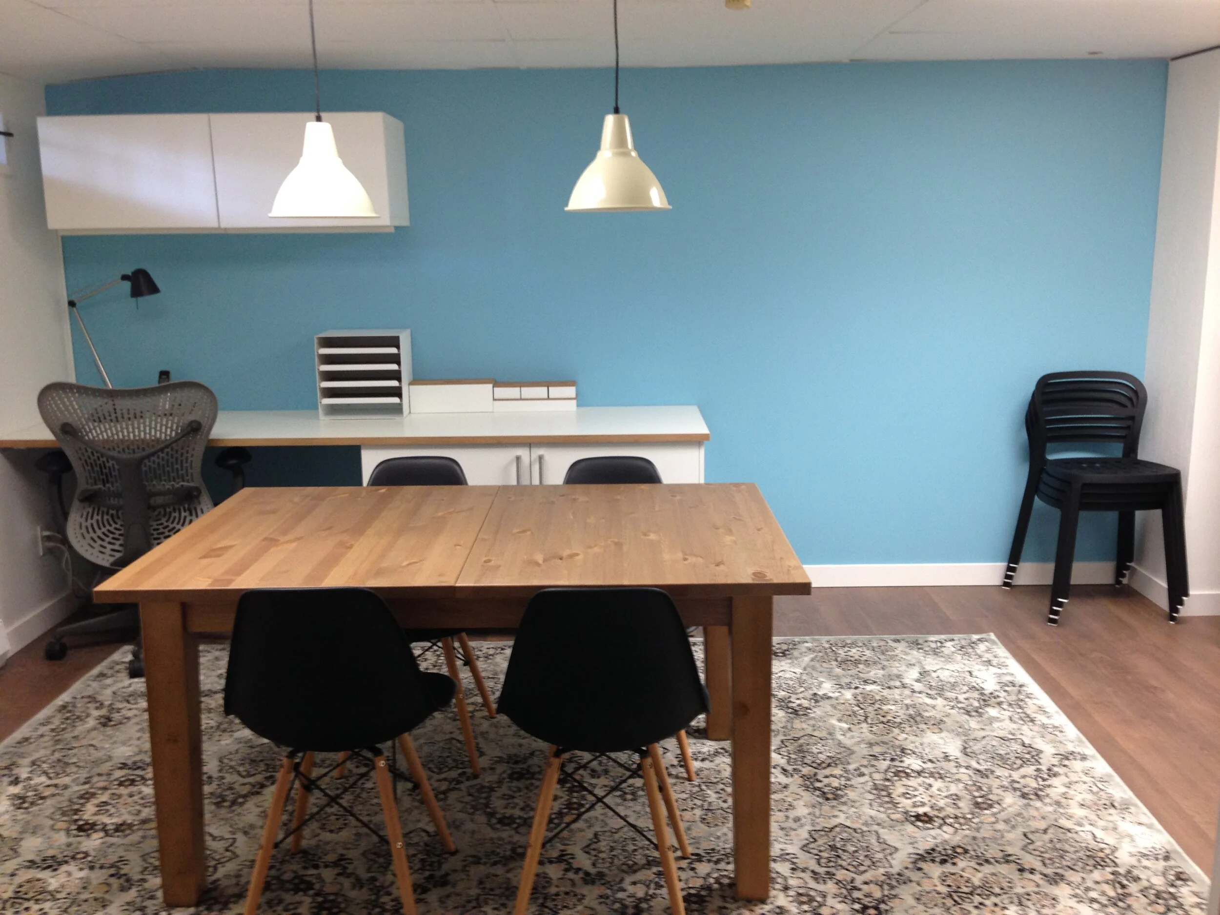 Blue painted wall with work/meeting table with extra seating and rug on floor.