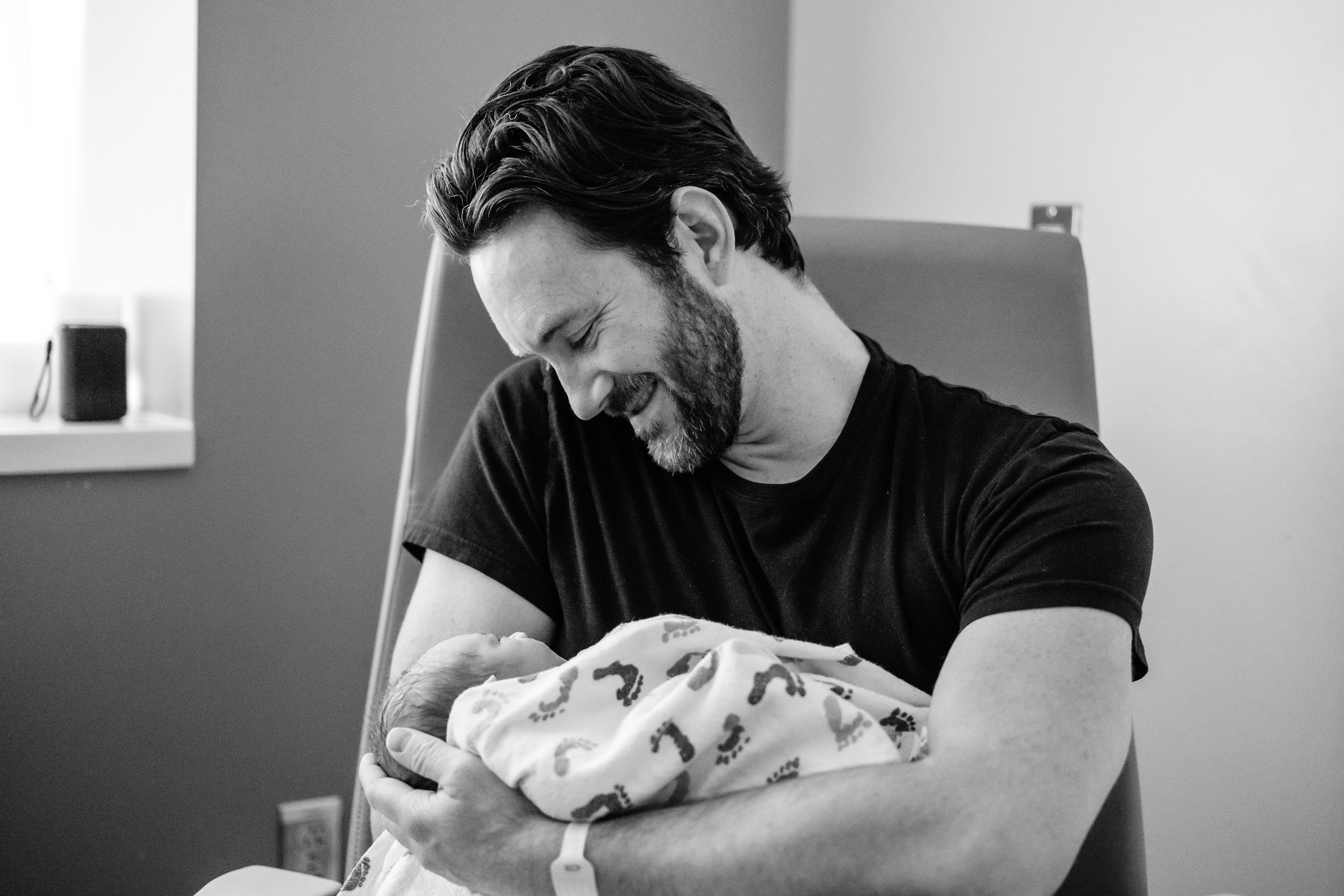 A father smiles and looks down lovingly while holding his newborn son in his arms.