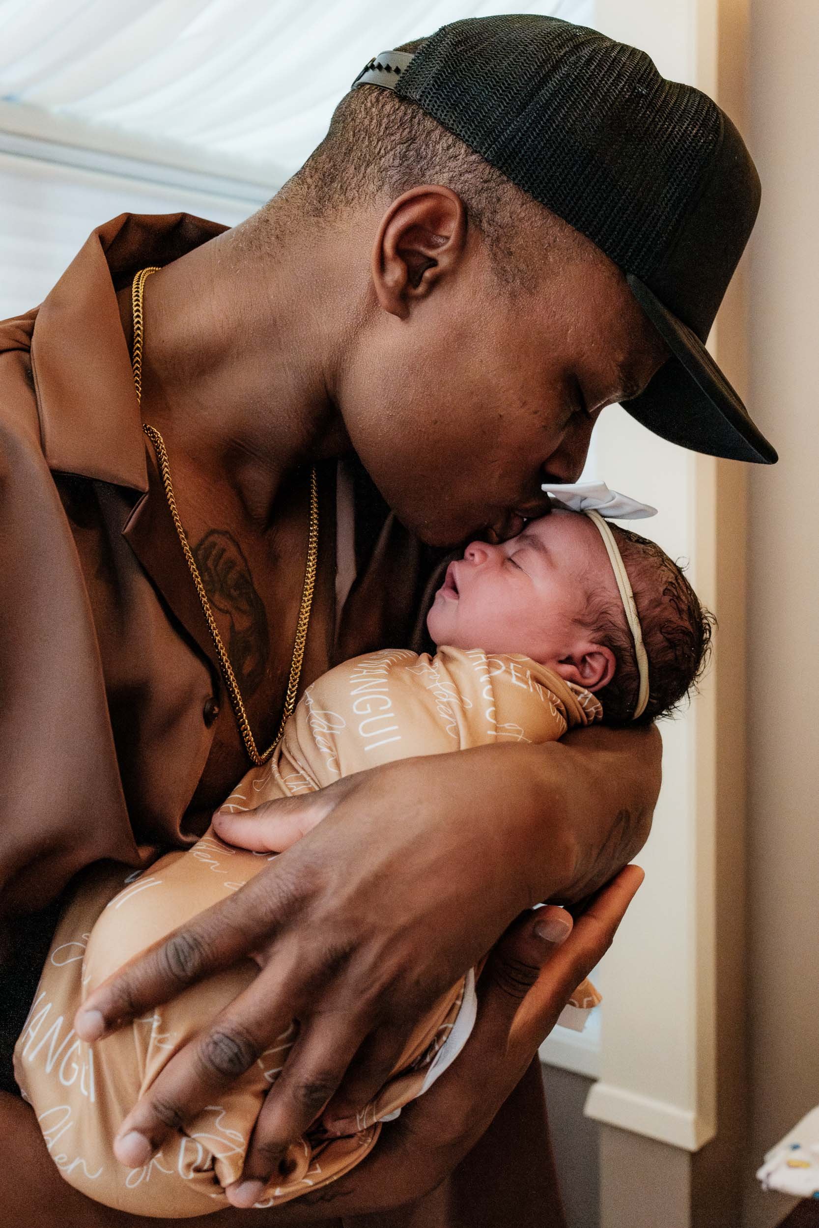 Black father kisses his newborn daughter on the forehead only a few short hours after birth.