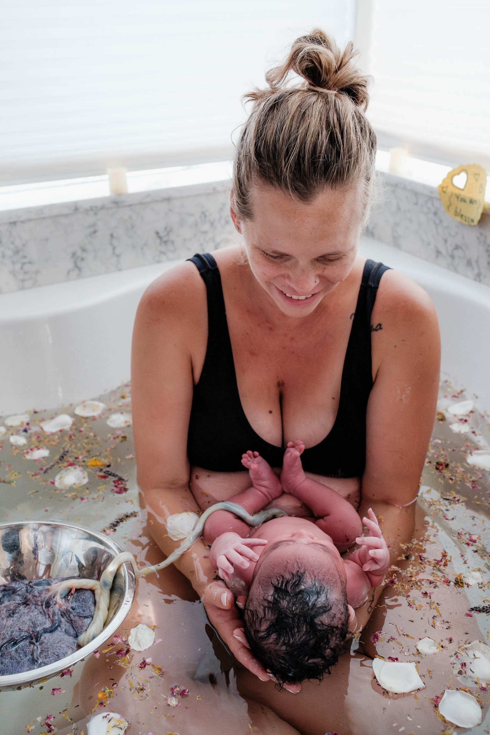 Mother and baby take an herbal bath together fresh after birth. Baby is still connected to their placenta.