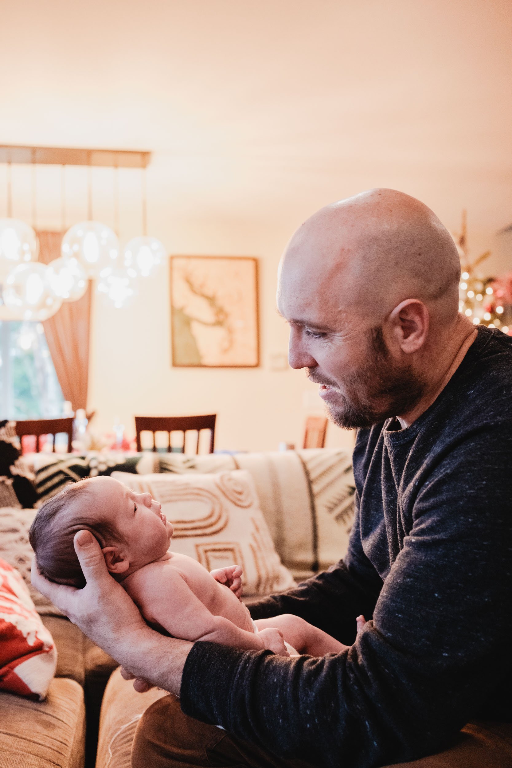 White male holds his newborn son in his hands during a newborn session at home.