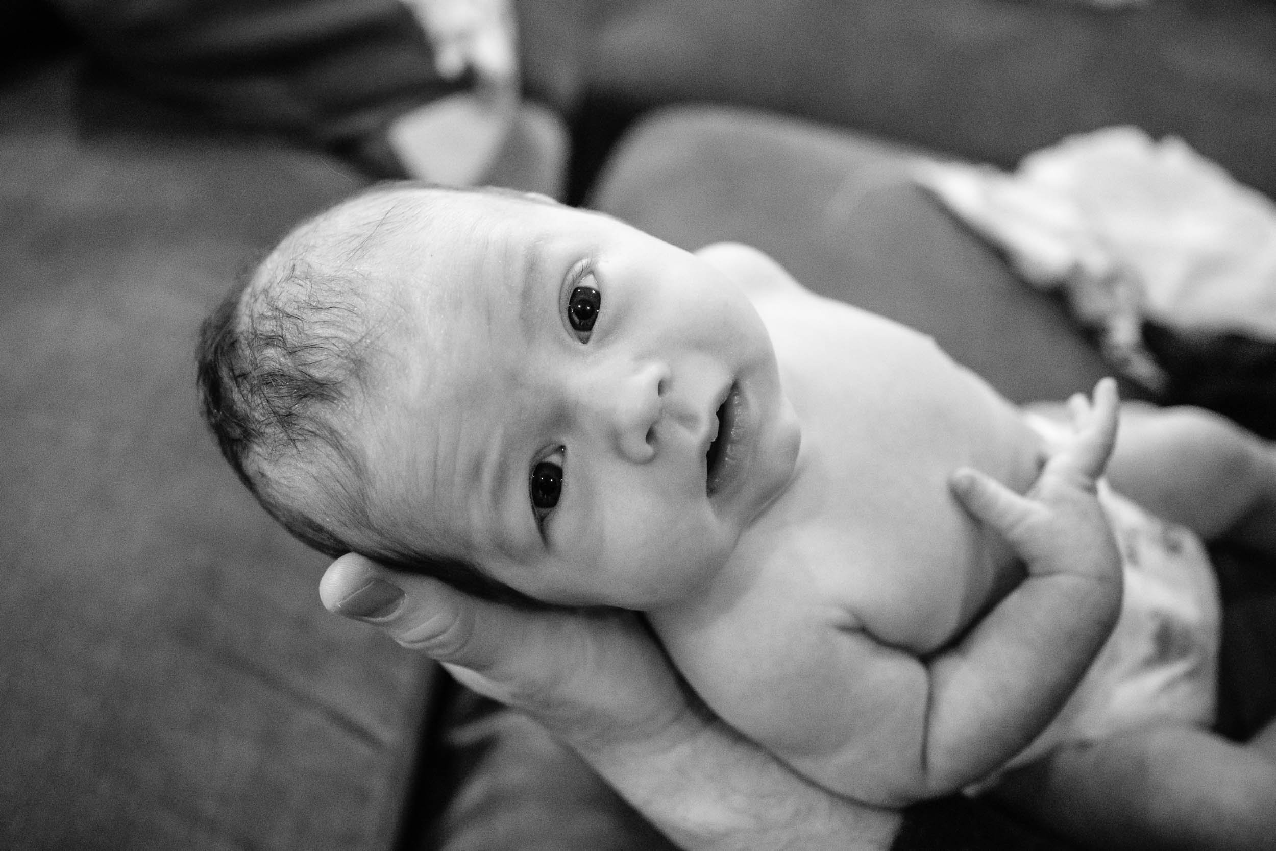 Newborn baby boy looks up at the camera while resting in his father's hands.