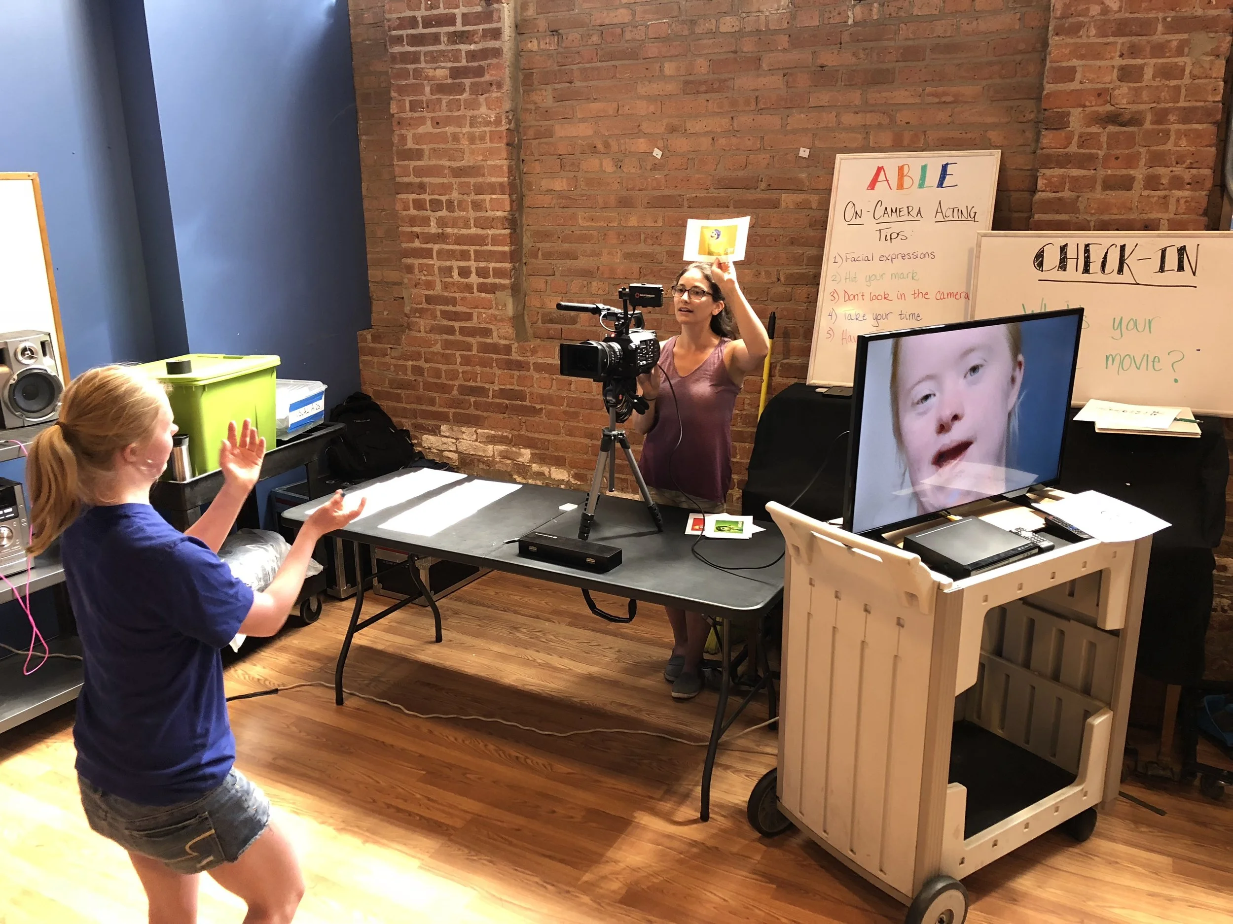Young actor in studio with camera, monitor shows expression, brick wall, acting tips displayed.