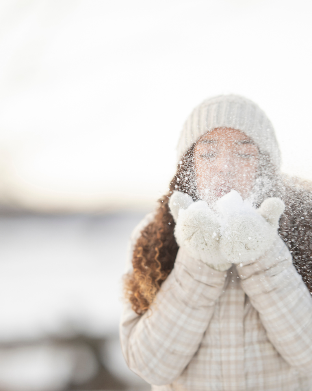 Woman in outdoor winter gear blowing snow at the camera