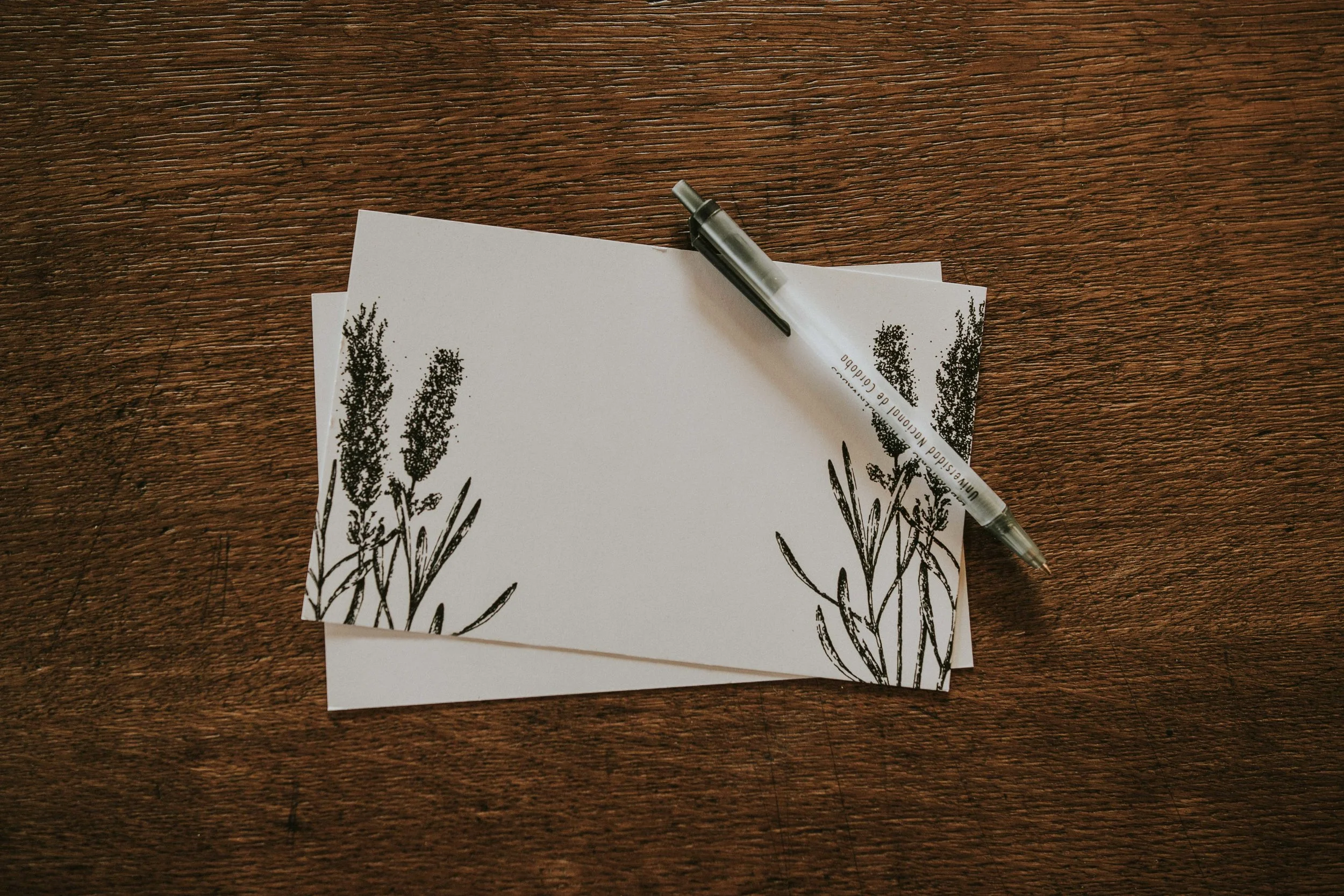 Blank card with floral design and pen sitting on a wooden desk.
