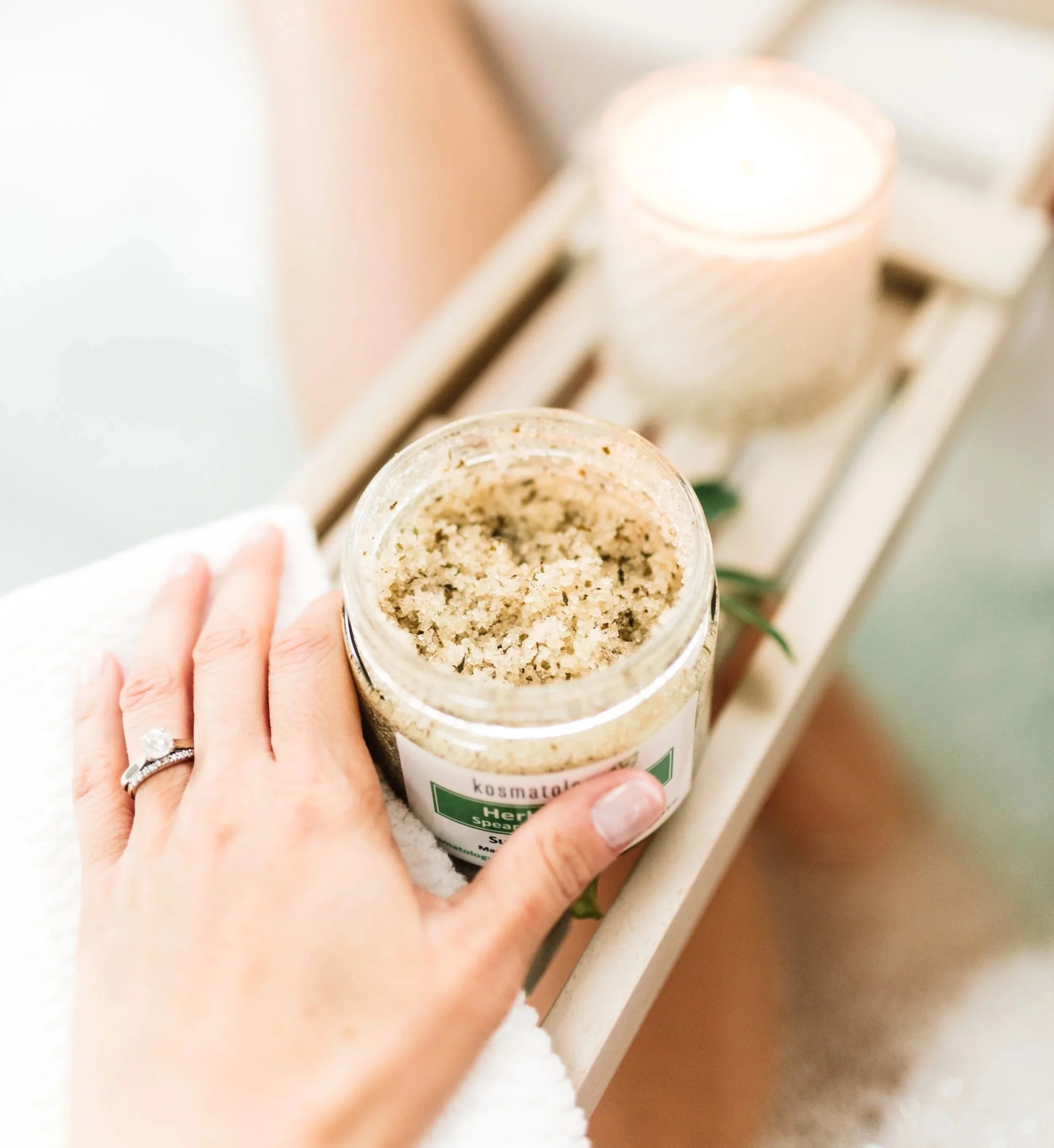 Kosmatology Herbal Fresh sugar scrub open on a bath tray with a hand holding it.
