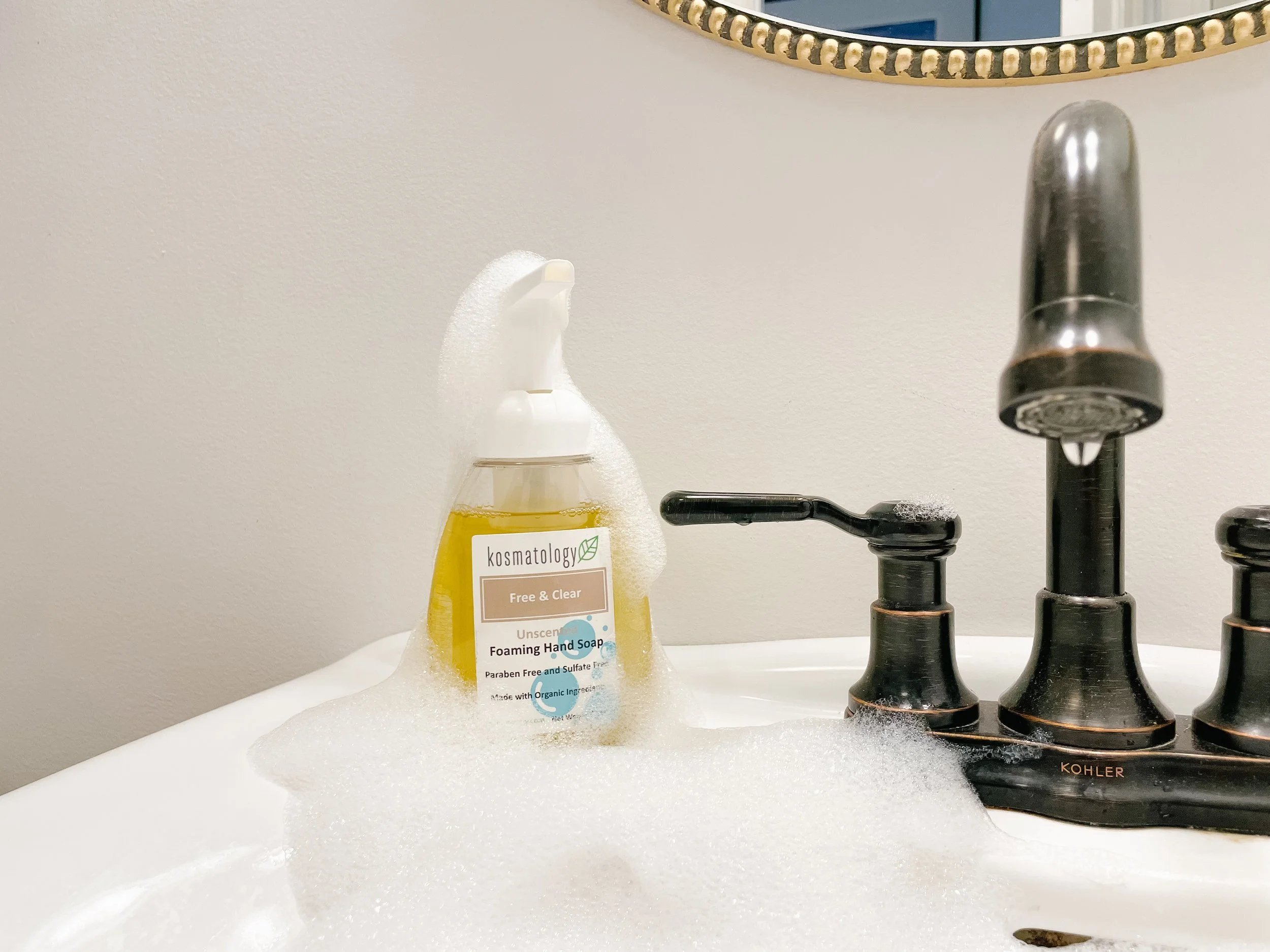 Kosmatology Free & Clear soap sitting on a bathroom sink covered in bubbles.