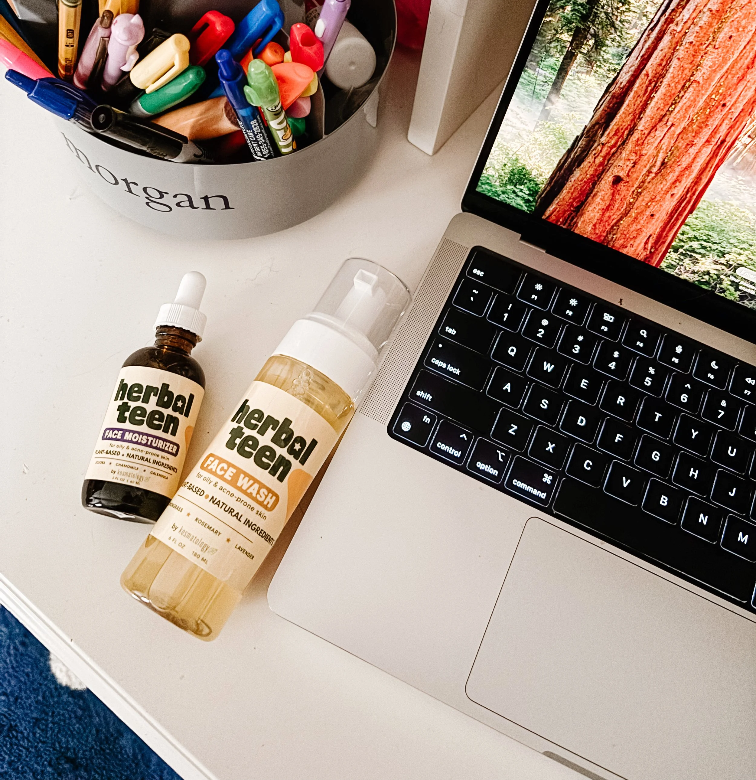 Herbal Teen by Kosmatology face wash and moisturizer  on a desk next to a computer and pen holder.