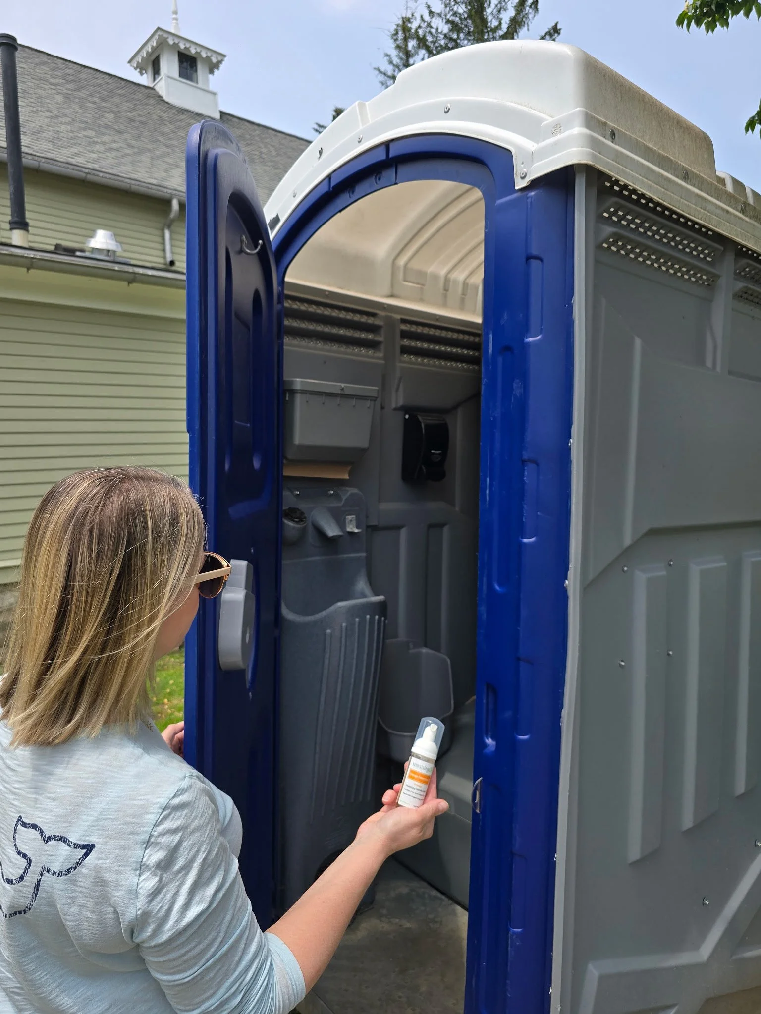 Woman entering a Port a potty holding Kosmatology travel hand soap